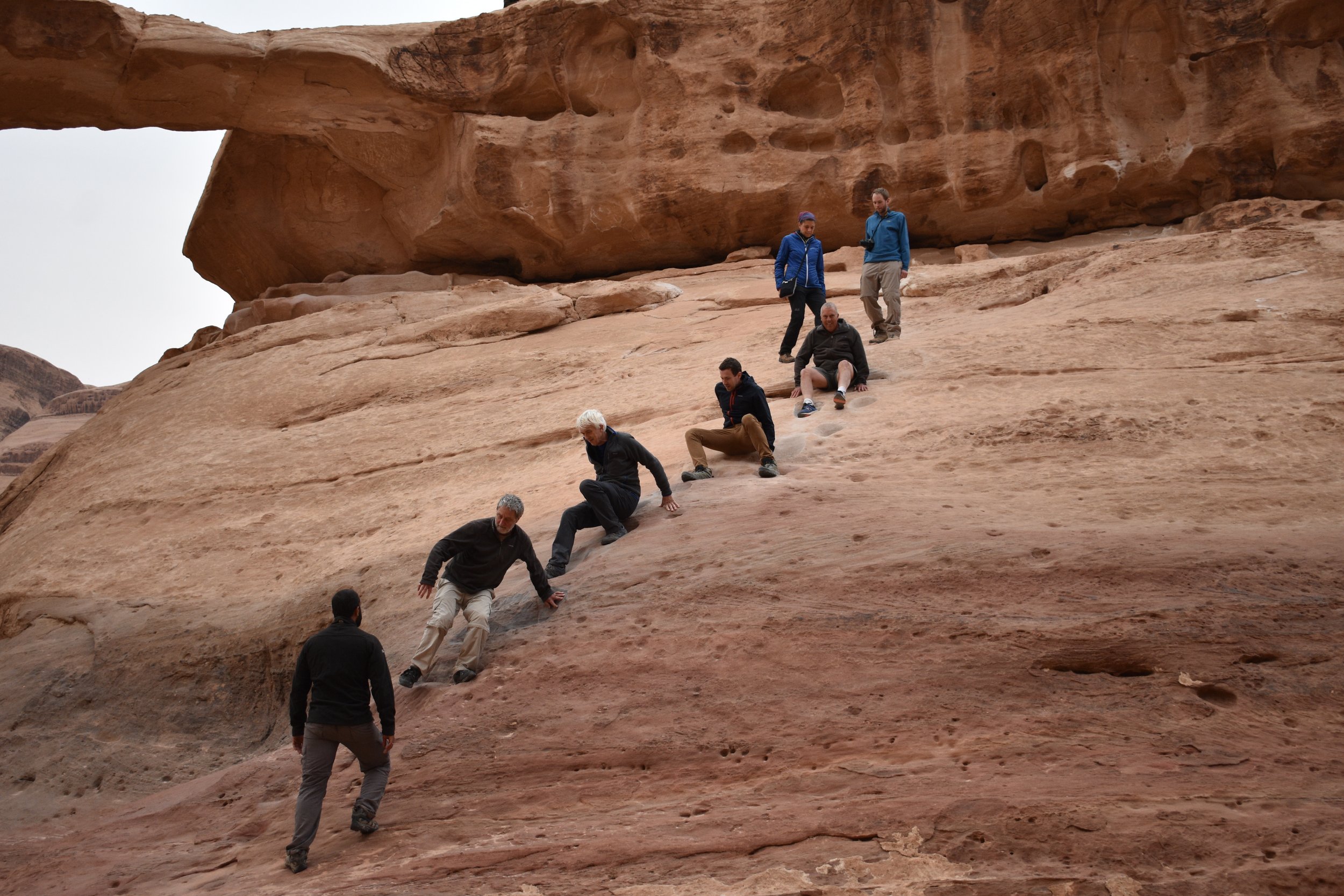 Group of people sliding down a rock slope in a desert landscape.