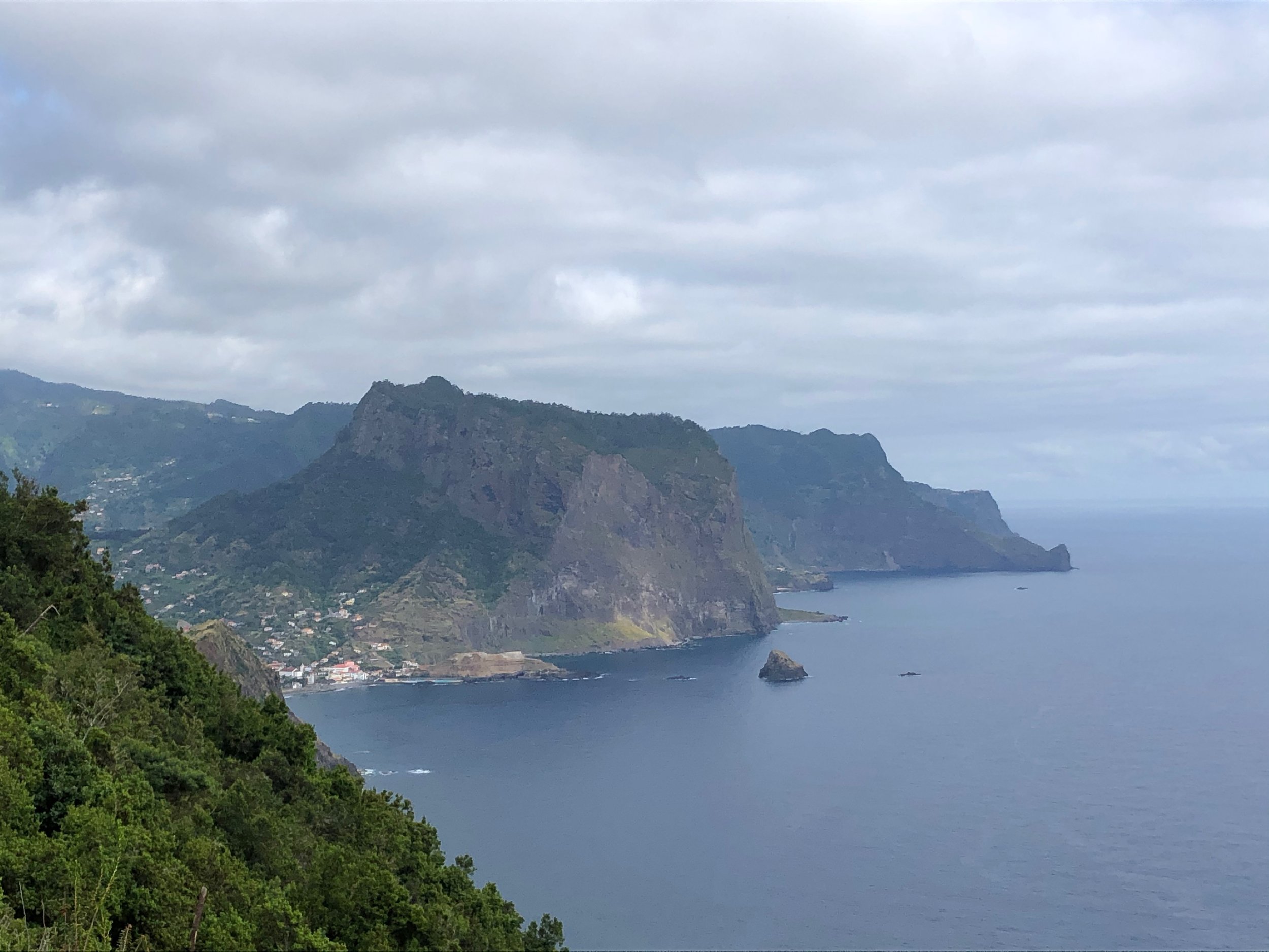 Panoramic view of lush green cliffs overlooking a calm ocean under a cloudy sky.