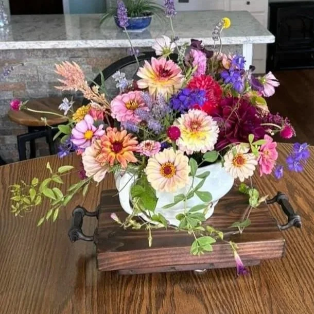 A colorful bouquet of mixed flowers in a white vase on a wooden tray on a dining table.