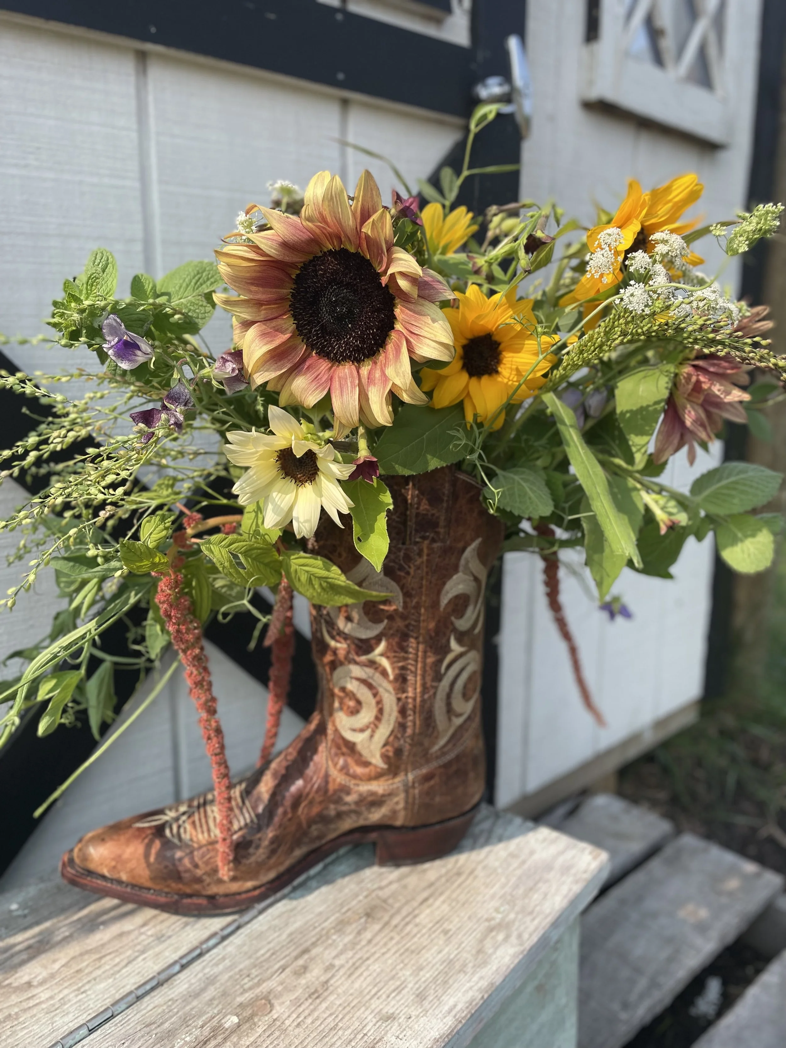 A bouquet of sunflowers, wildflowers, and greenery in a cowboy boot-shaped vase.