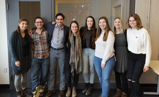 Eight lab members standing side by side indoors