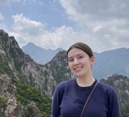 Young woman smiling outdoors with mountains and cloudy sky in the background