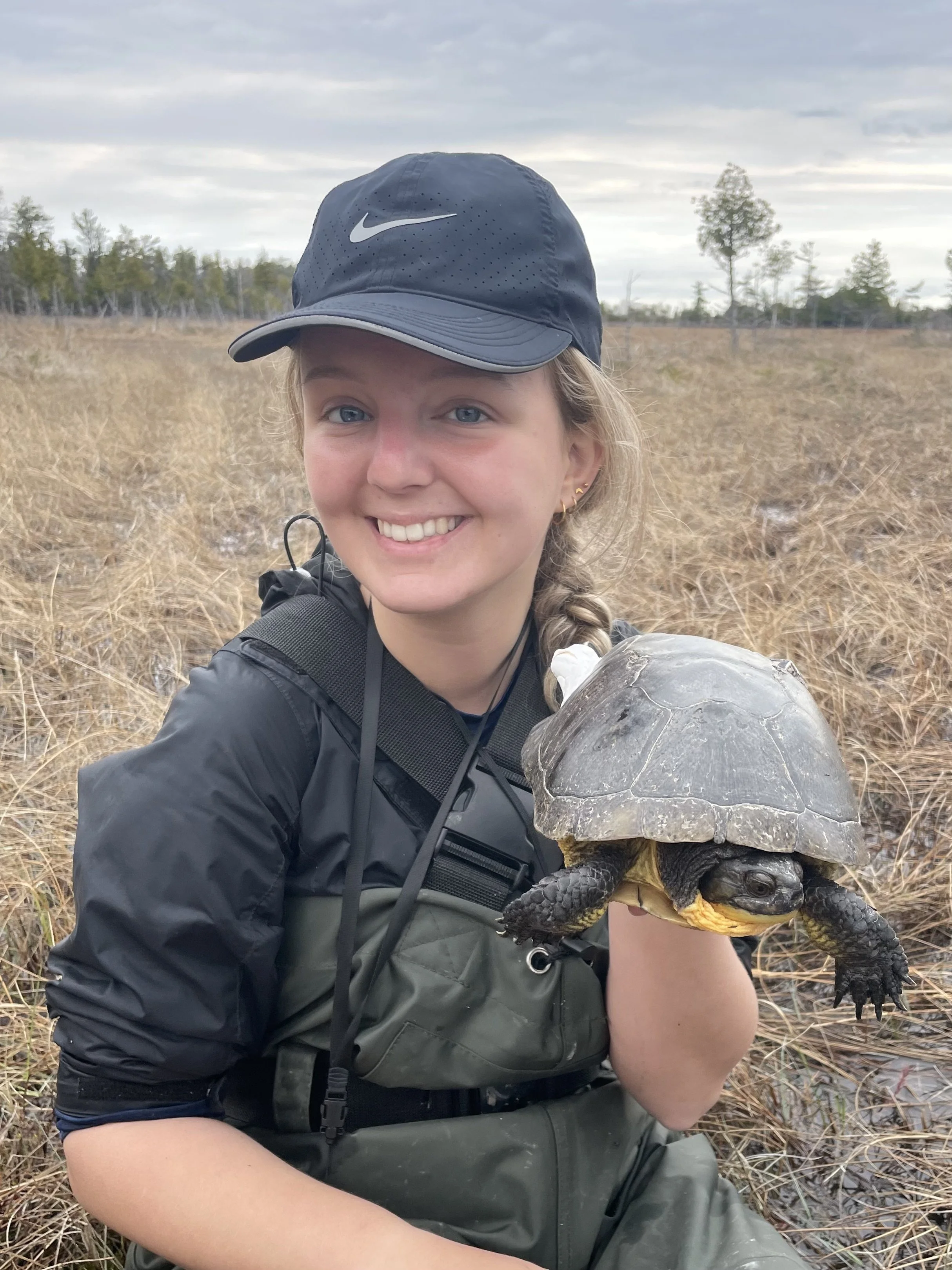 A young girl smiling and holding a turtle in a marshland area