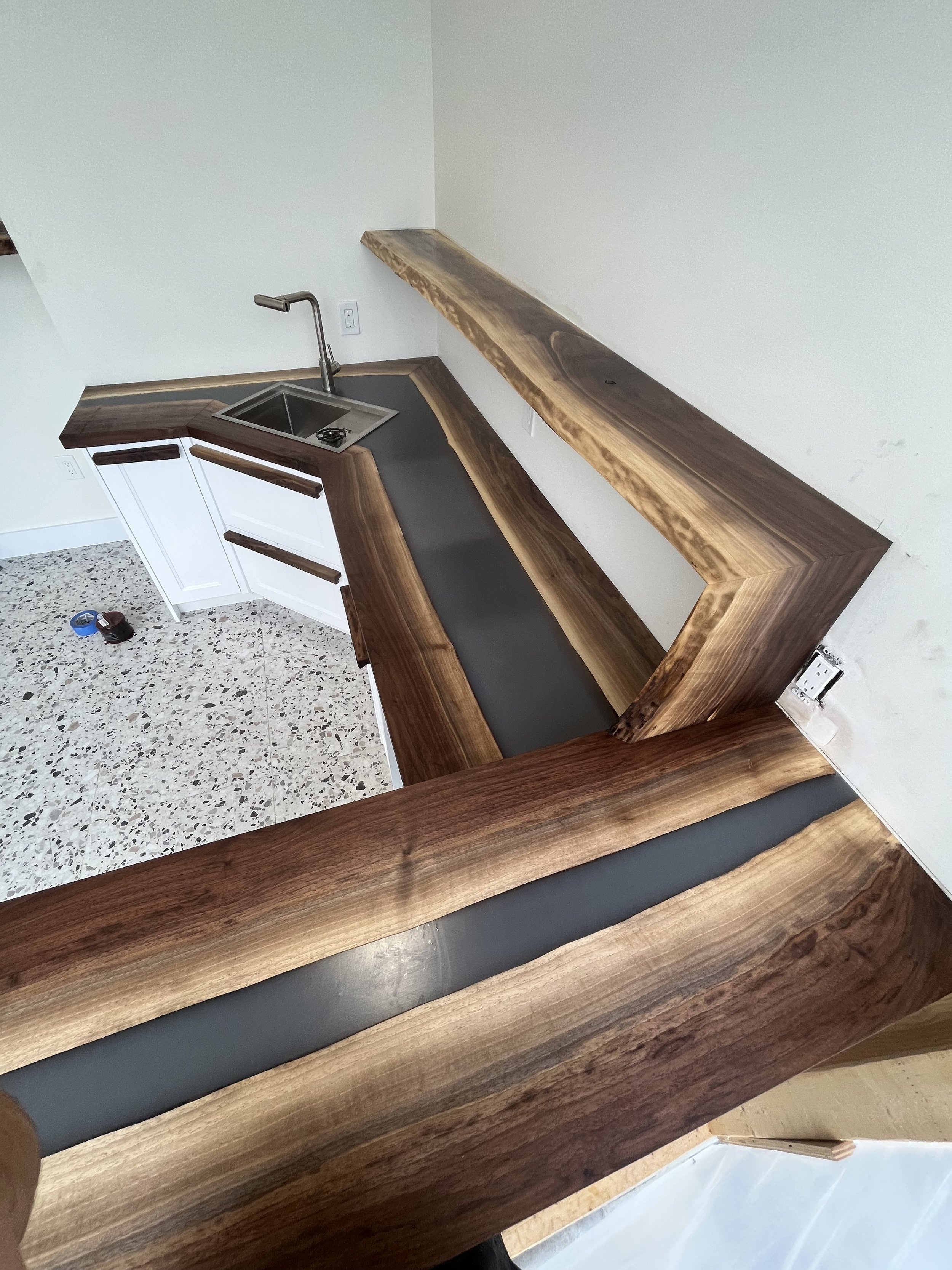 Kitchen with live edge wood countertops and a stainless steel sink on white cabinets. Terrazzo flooring and minimalist design.