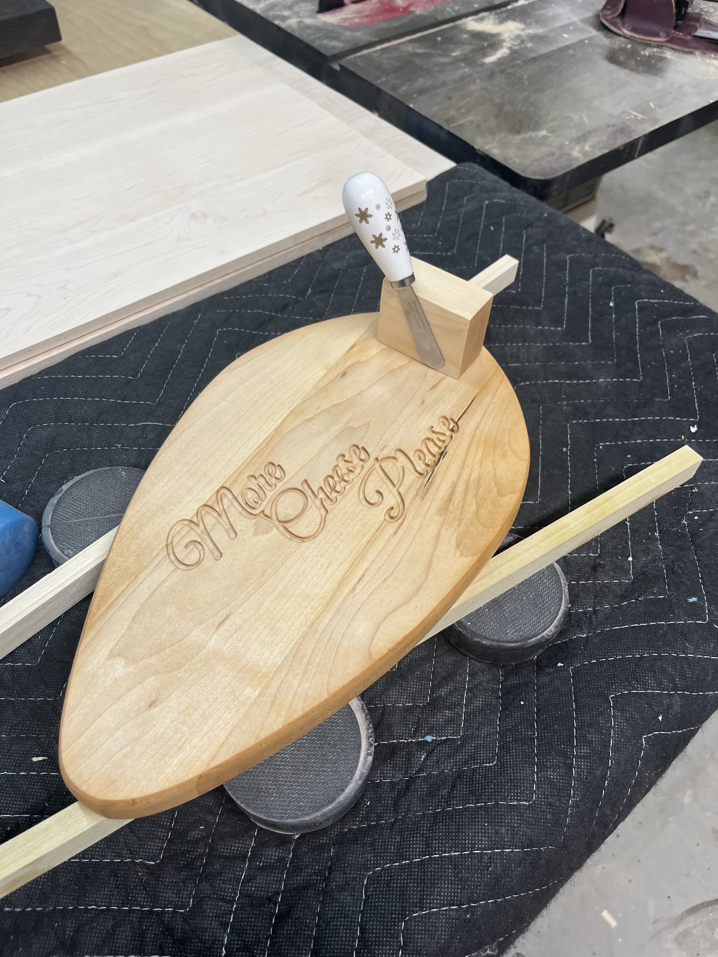 Wooden cheese board with "Make Cheese Please" engraved, topped with a decorative knife.