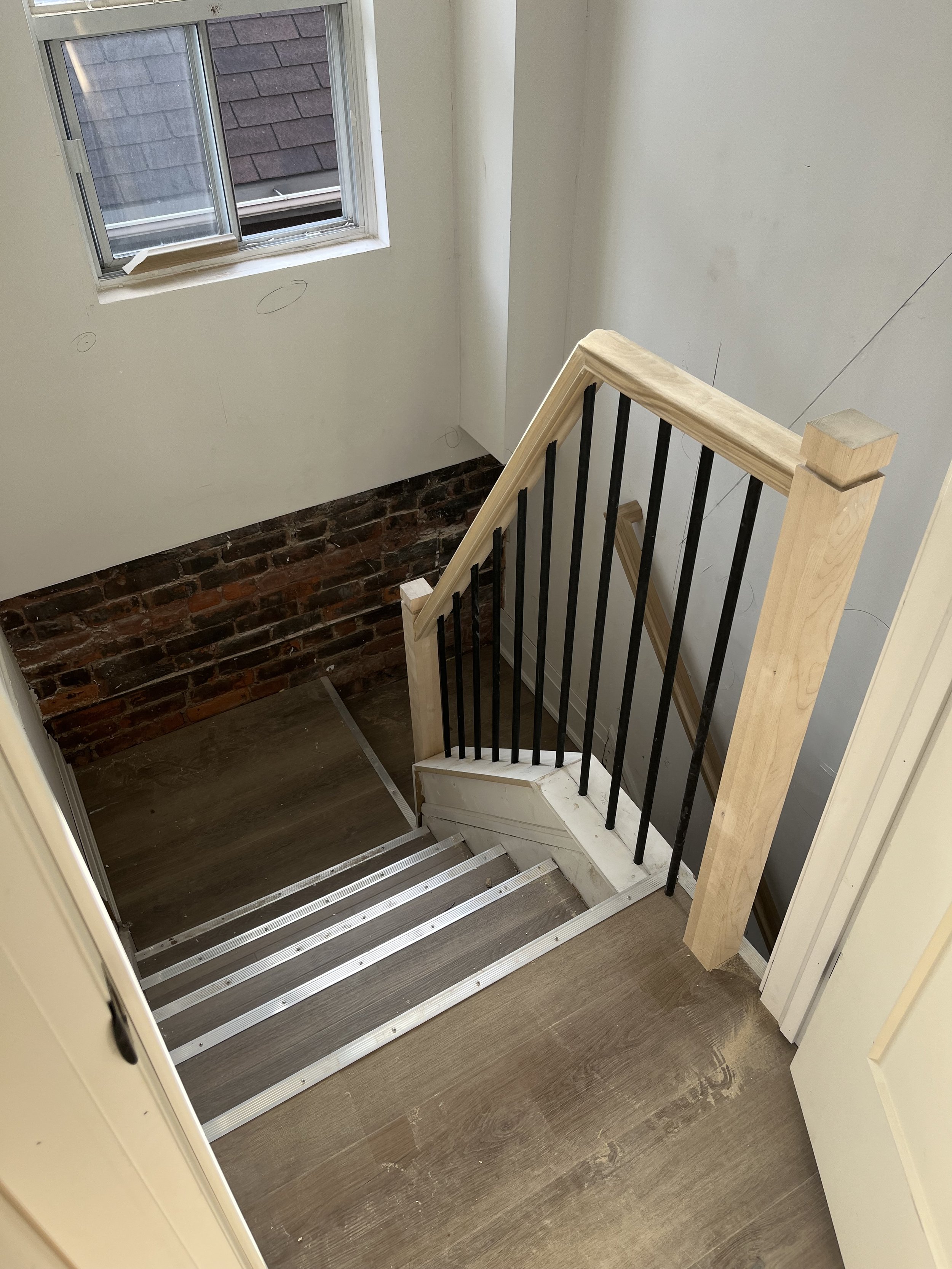 A wooden staircase with metal railings in a residential building, featuring a small window and exposed brick wall.