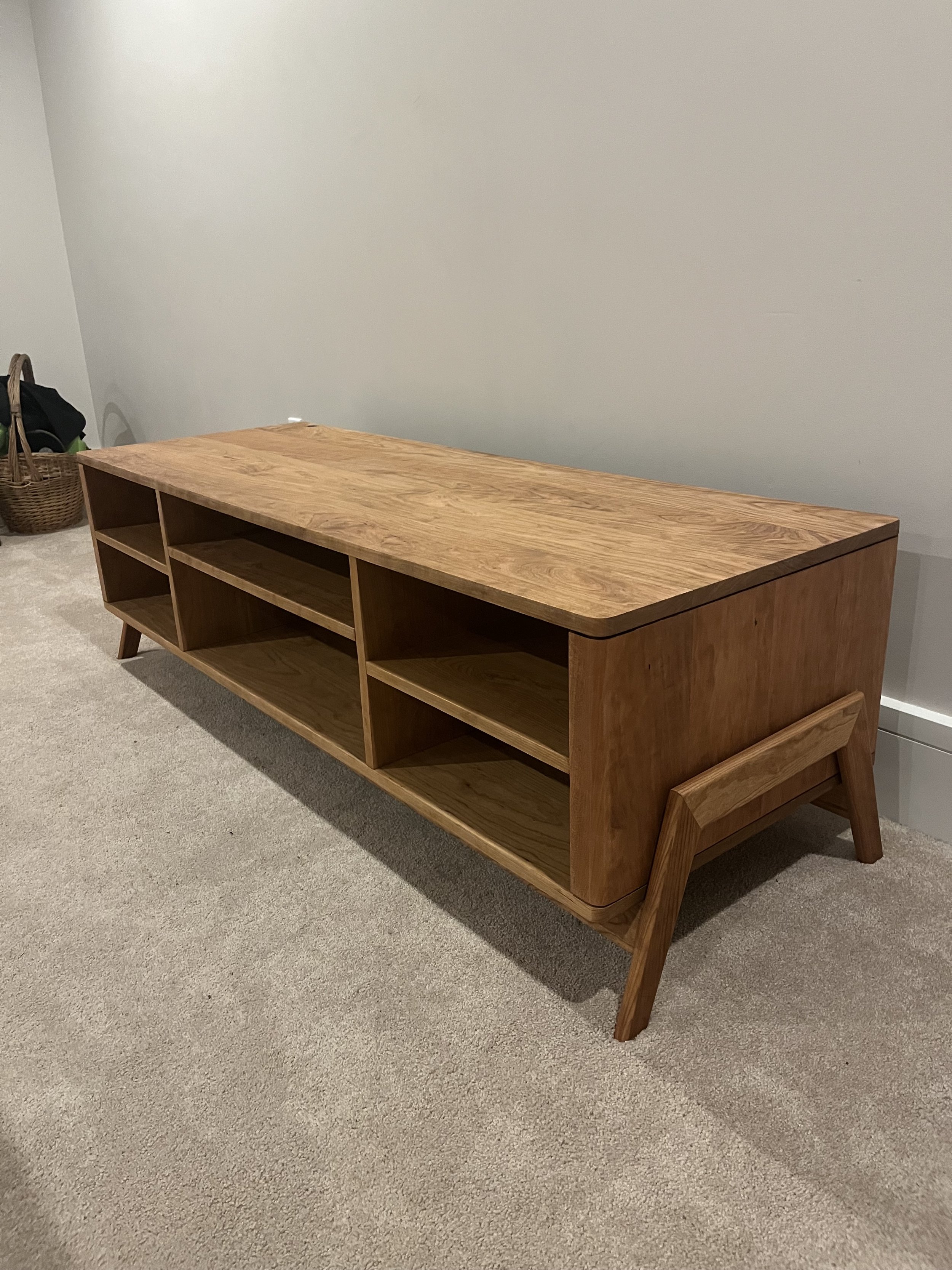 Wooden mid-century modern TV stand with open shelves on a carpeted floor.