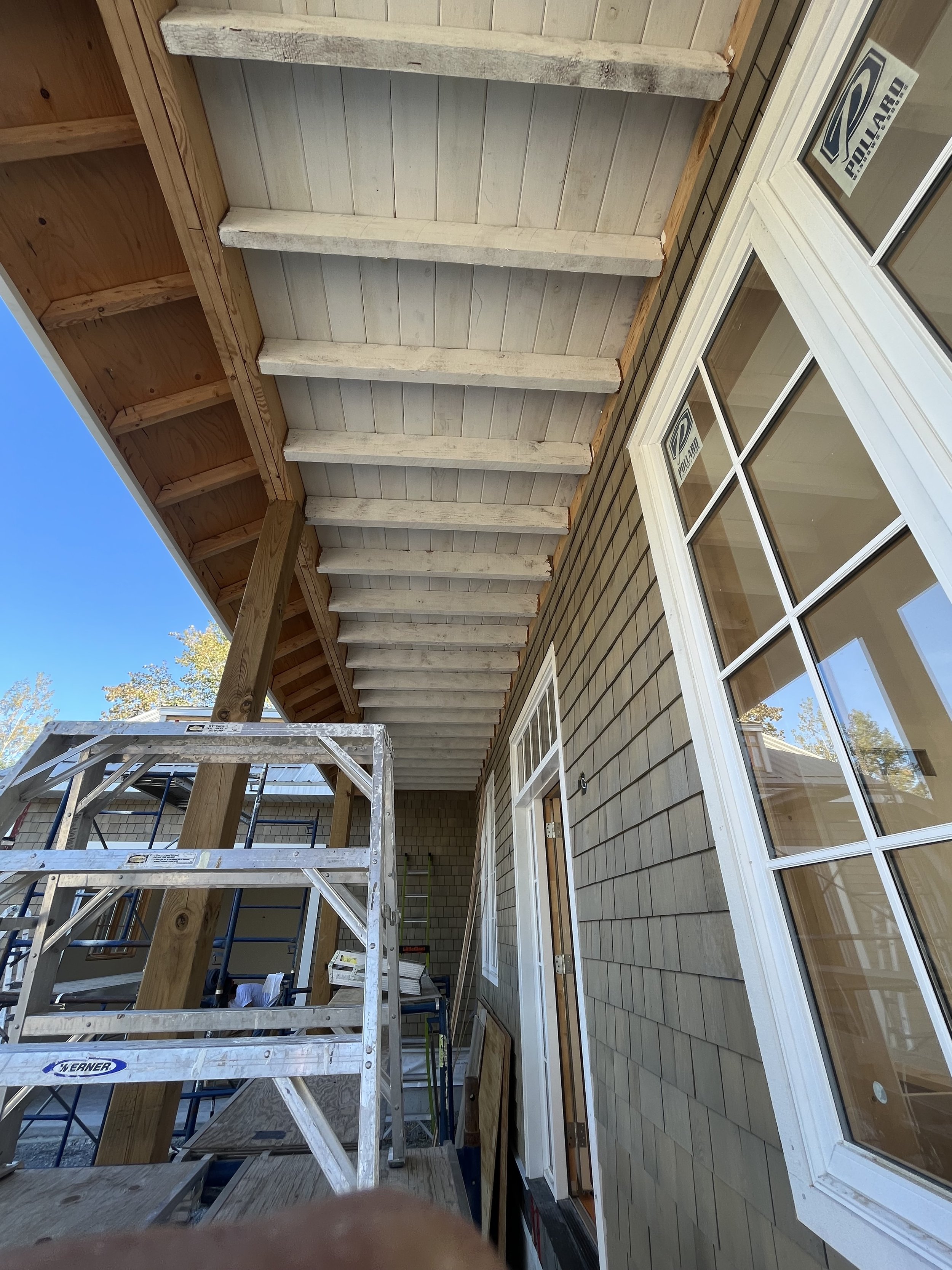 Building under construction with wooden porch roof, ladder, and windows.