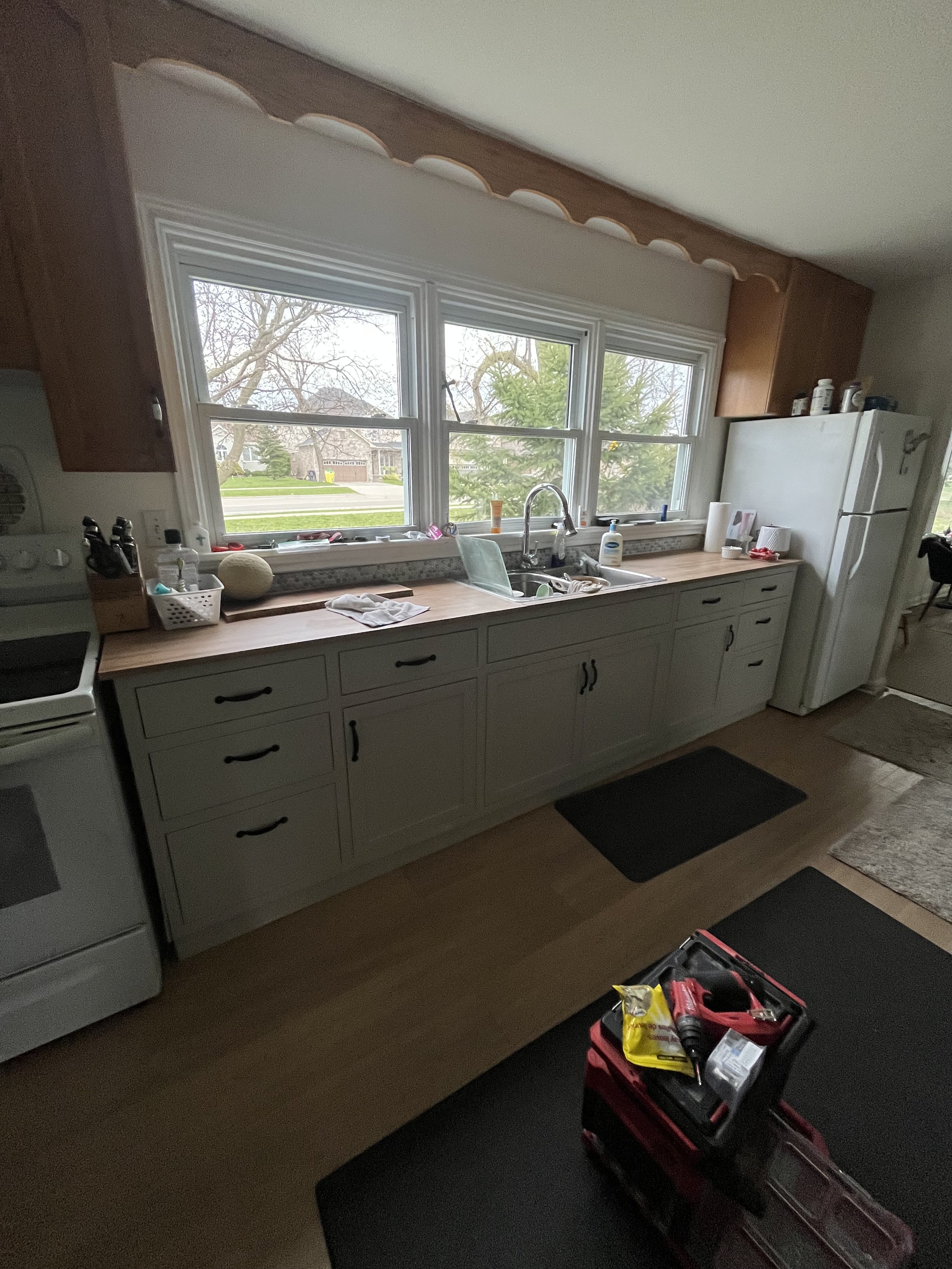 Kitchen with white cabinets, wooden countertop, large windows, and tools on the floor.