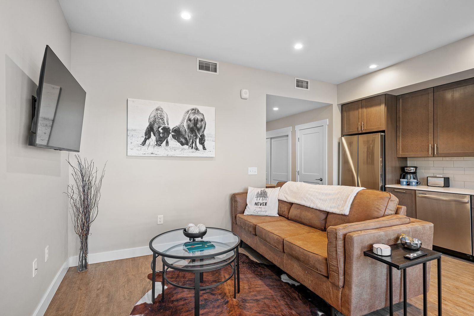 Living room and kitchen of a BozemanBnB managed condo in downtown Bozeman, with a leather sofa and bison artwork.