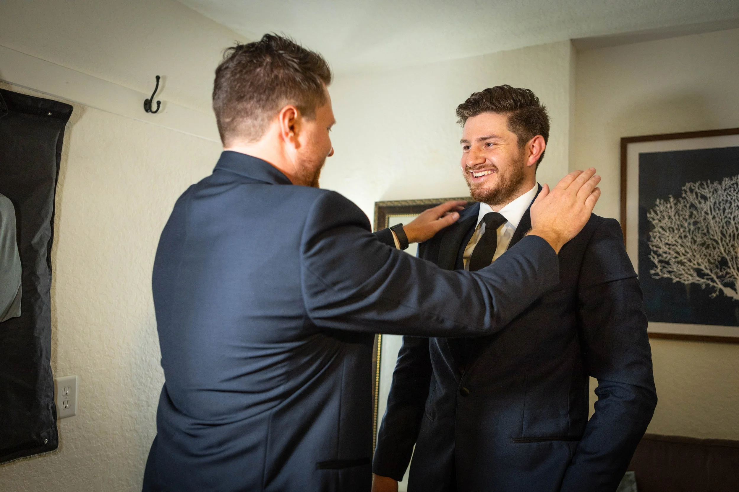 Two men in formal suits smiling and engaging in a friendly conversation indoors.