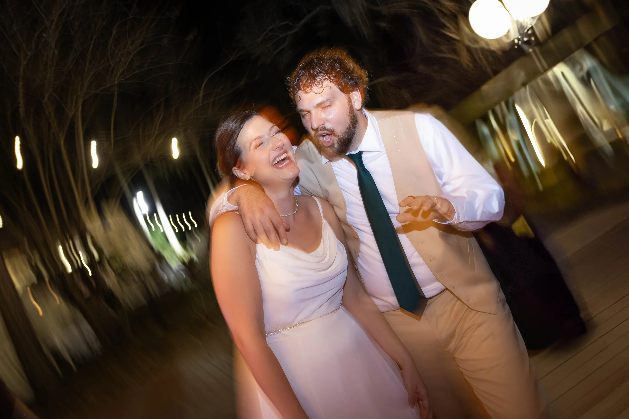 A bride and groom dancing closely at their wedding reception, laughing and enjoying the moment under warm lighting.