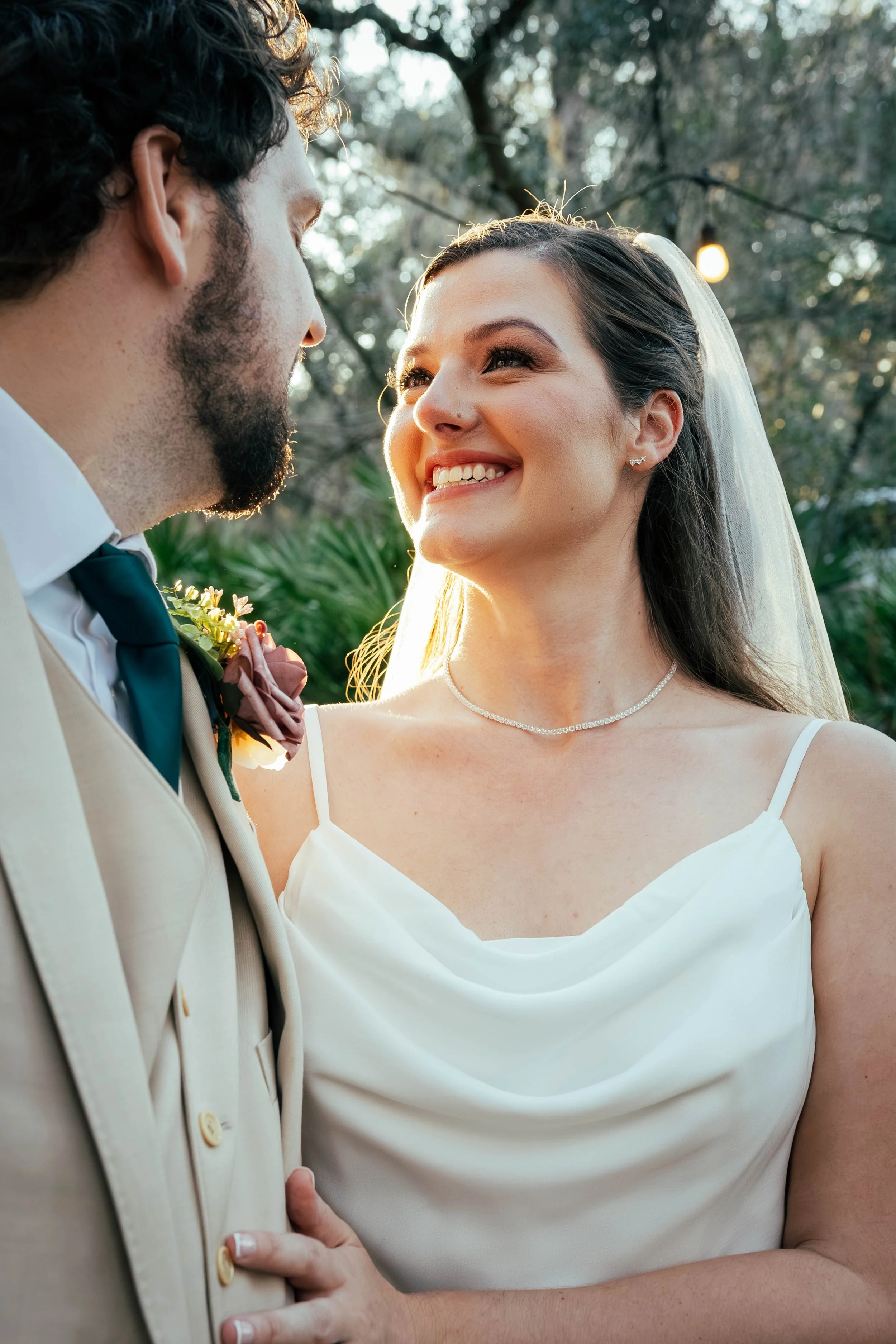Close-up of a bride and groom looking into each other's eyes outdoors with trees in the background, during their wedding.