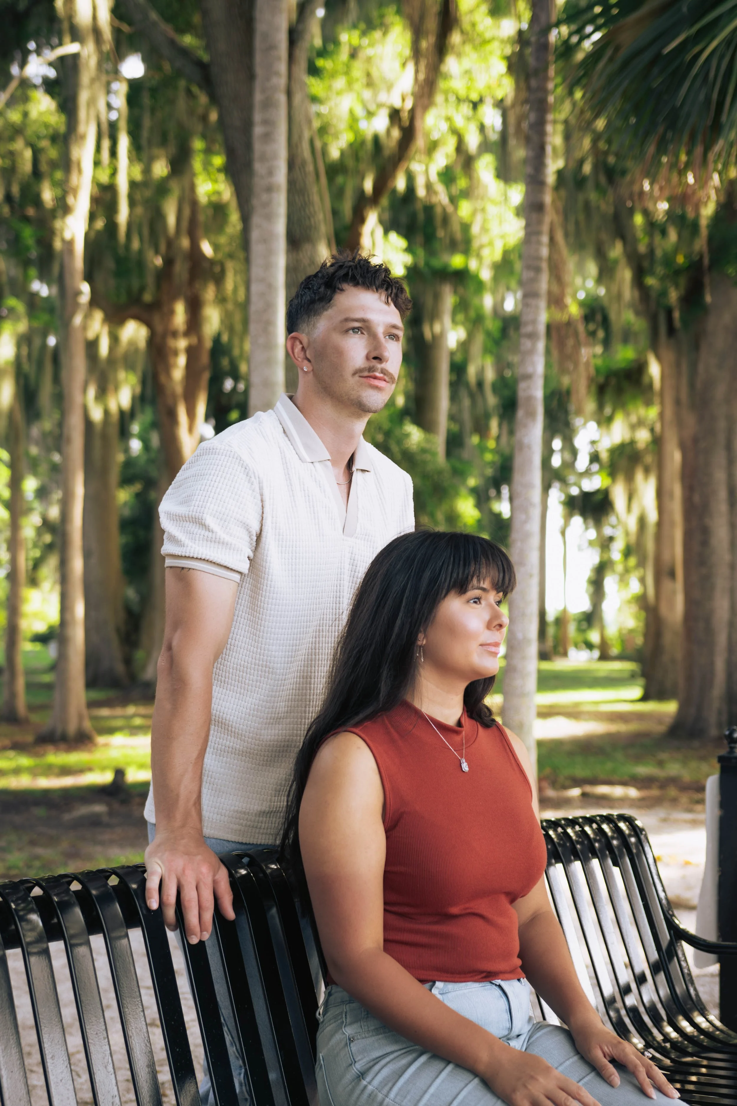 A man and a woman sitting on a park bench surrounded by trees.