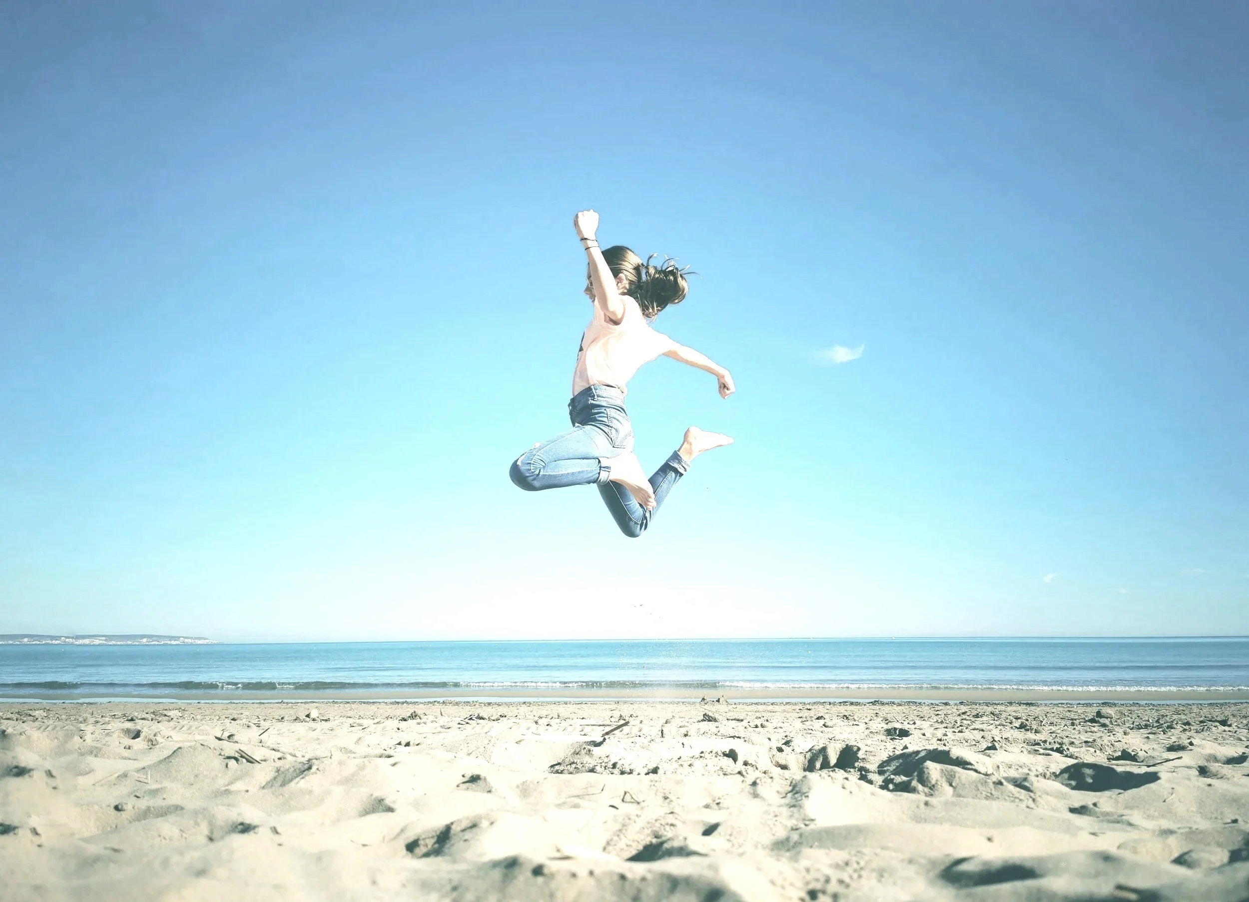 Eine Person springt in die Luft an einem Strand unter einem klaren blauen Himmel.