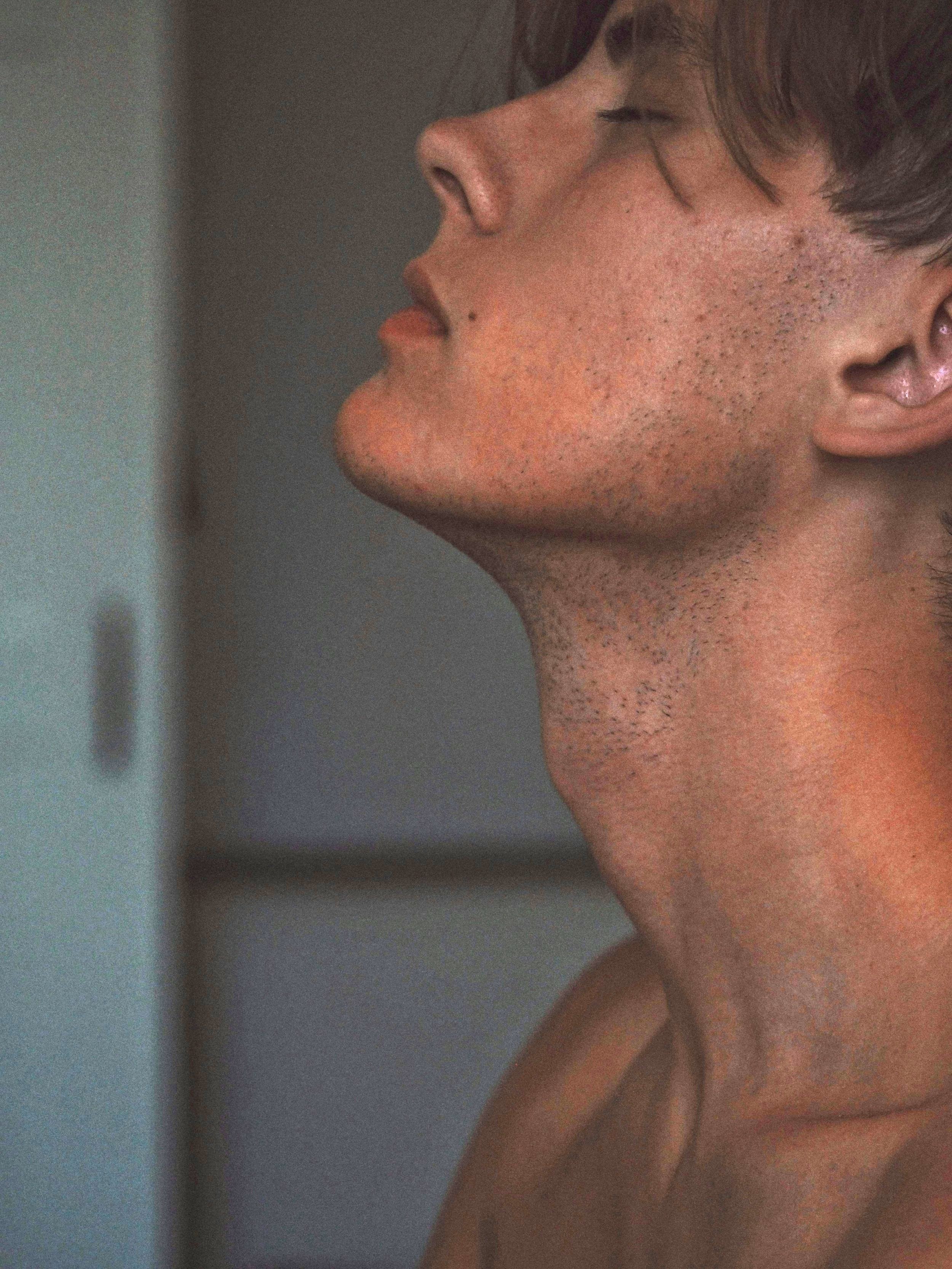 Nahaufnahme eines jungen Mannes in Seitenansicht mit geschlossenen Augen, sichtbare Hautporen, leichte Gesichtsbehaarung und Nacken.