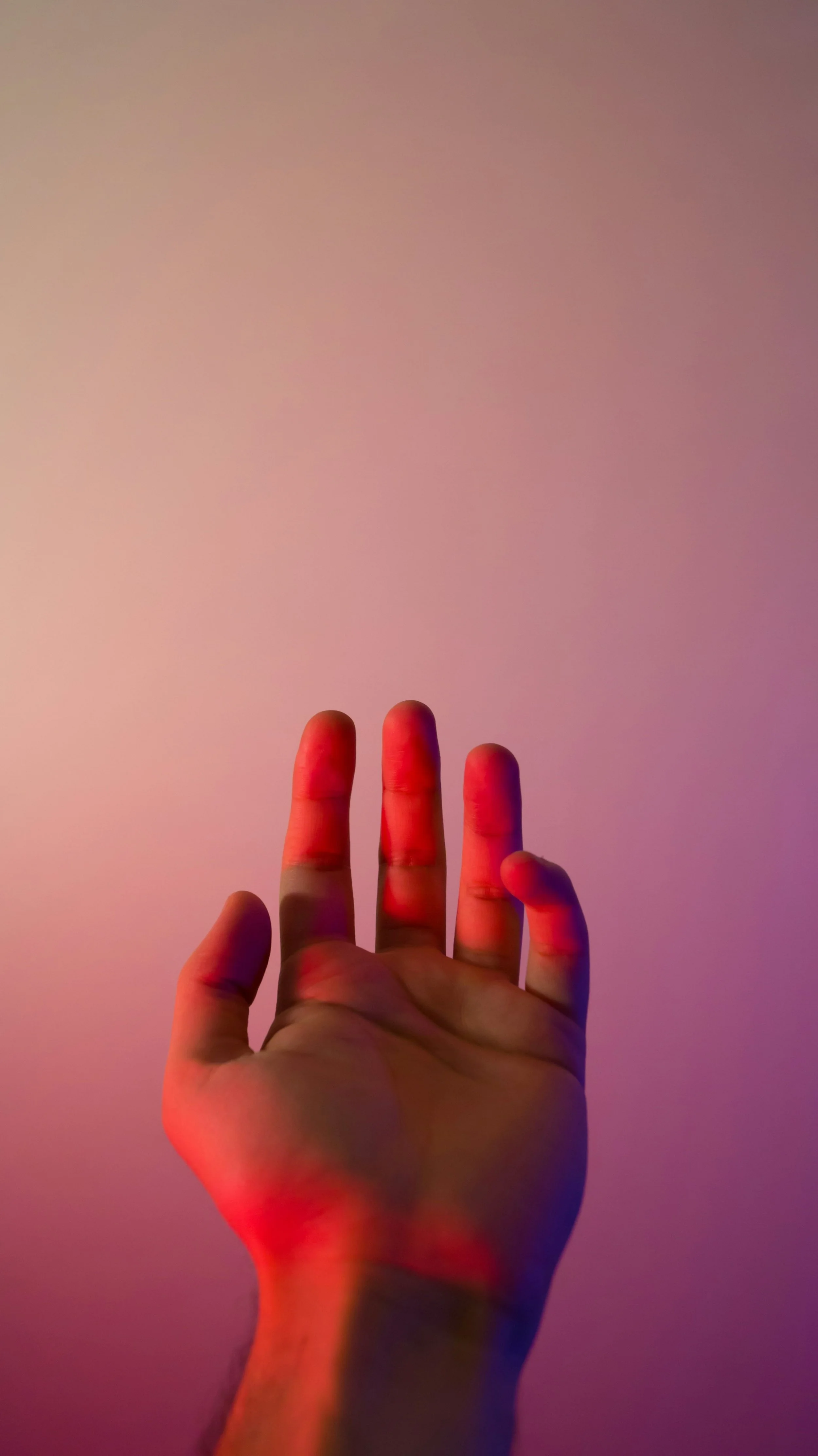 Eine Hand mit ausgestreckten Fingern vor einem pinken und blauen Hintergrund, teilweise im Schatten, der eine künstlerische Lichteffekten erzeugt.