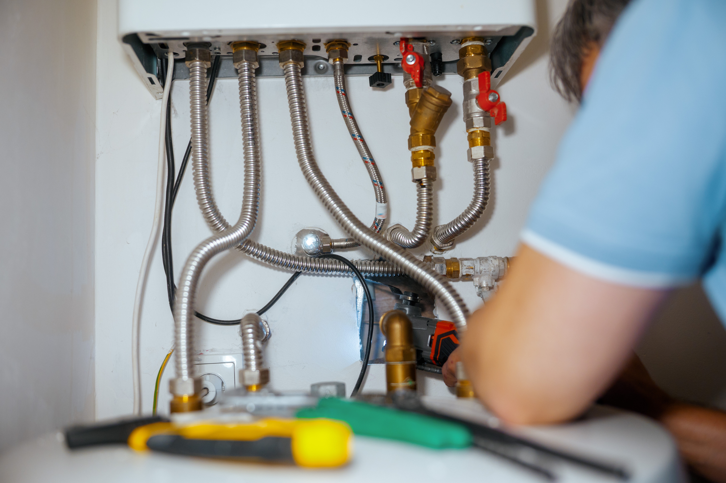 Plumber installing or repairing plumbing pipes while working on a tank less water heater, with various metal and plastic pipes and fittings visible.