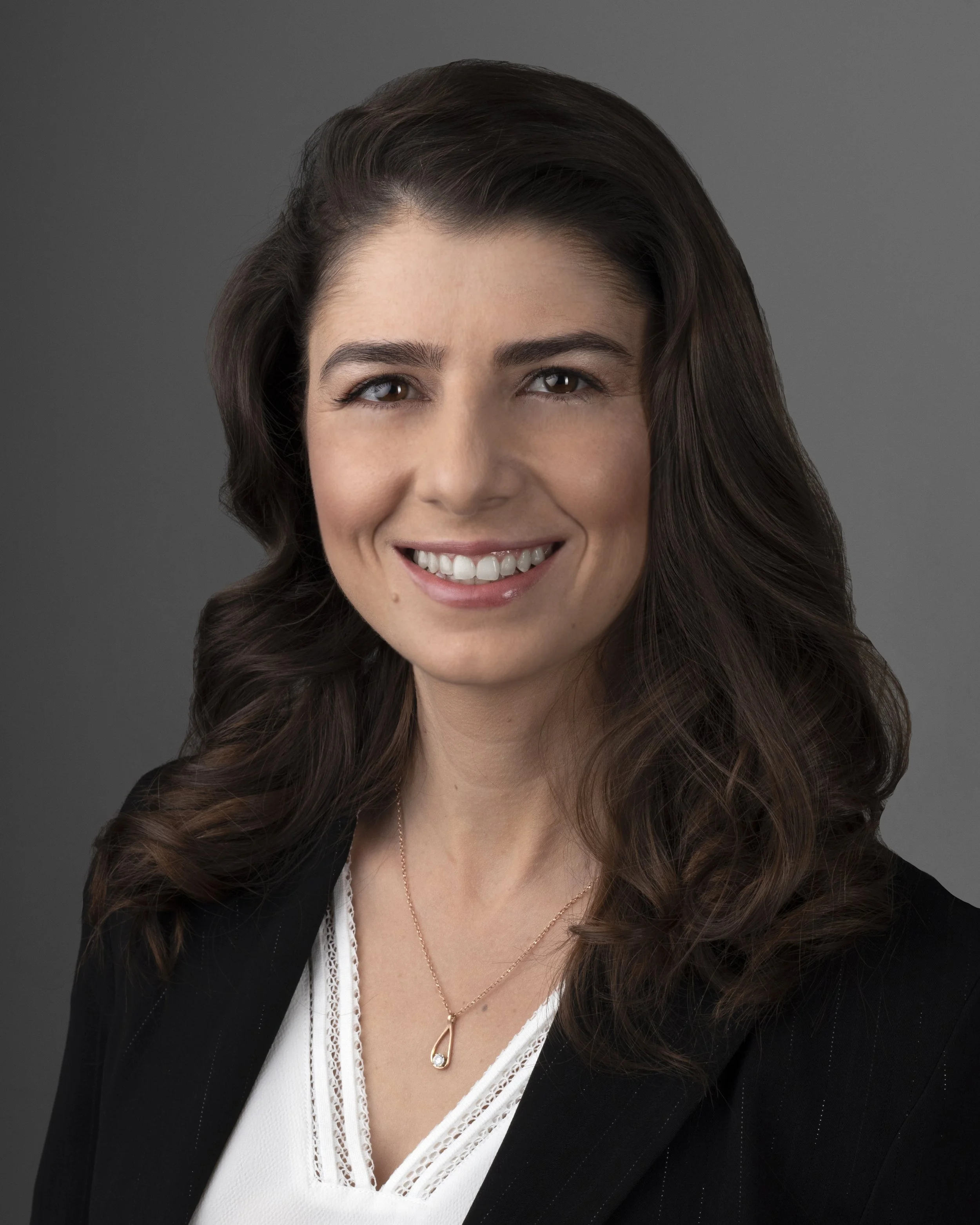 A woman with shoulder-length dark hair smiling outdoors in front of a green and blurred natural background.