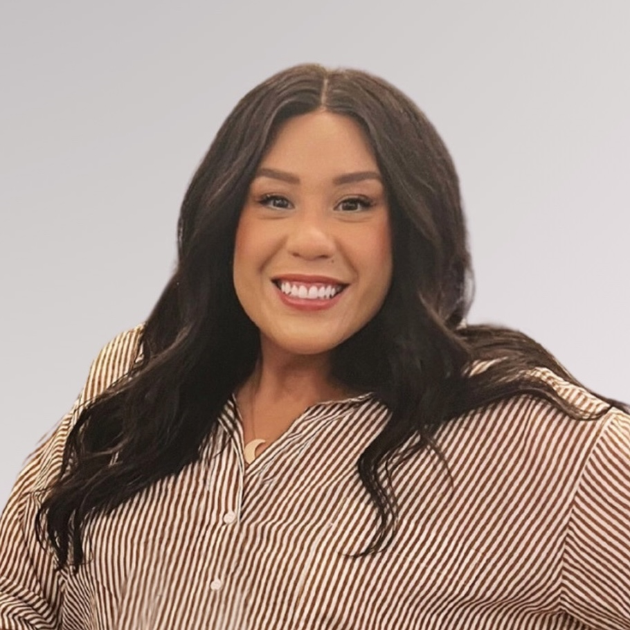 Tiffany, a light-skinned Latina with long dark wavy hair, smiling warmly at the camera. She's wearing a brown and white striped button-up shirt against a light gray background in a professional headshot-style photo