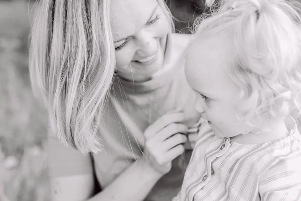 Black and white photo of a smiling woman with shoulder-length hair, interacting with a young child with curly hair.
