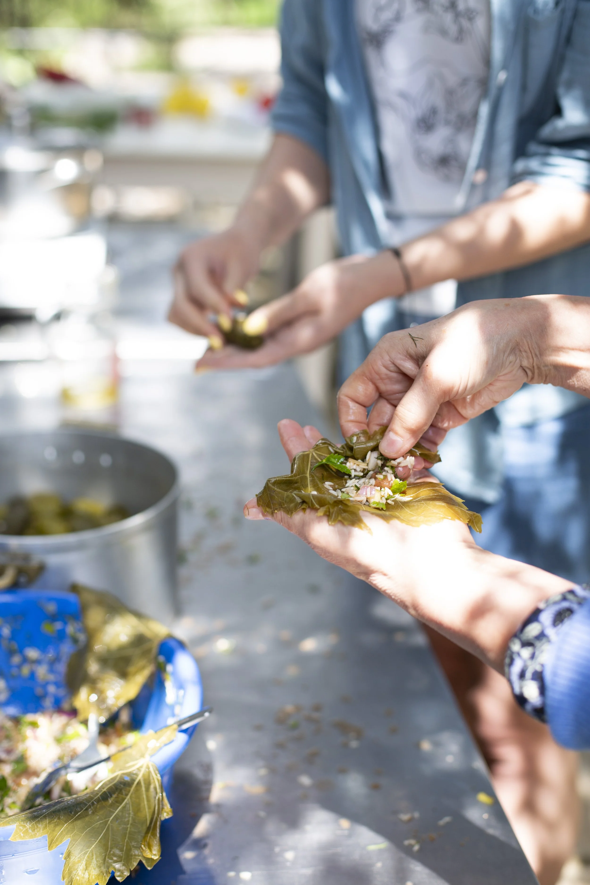 Kahden ihmisen kädet täyttävät viininlehtiä ja täyttävät niitä keitetyillä riisinuudeleilla ja vihanneksilla.