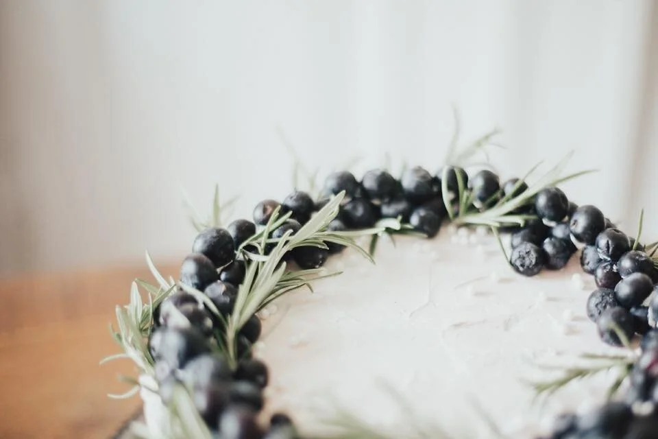 Close-up of a decorated cake with blueberries and rosemary on top.