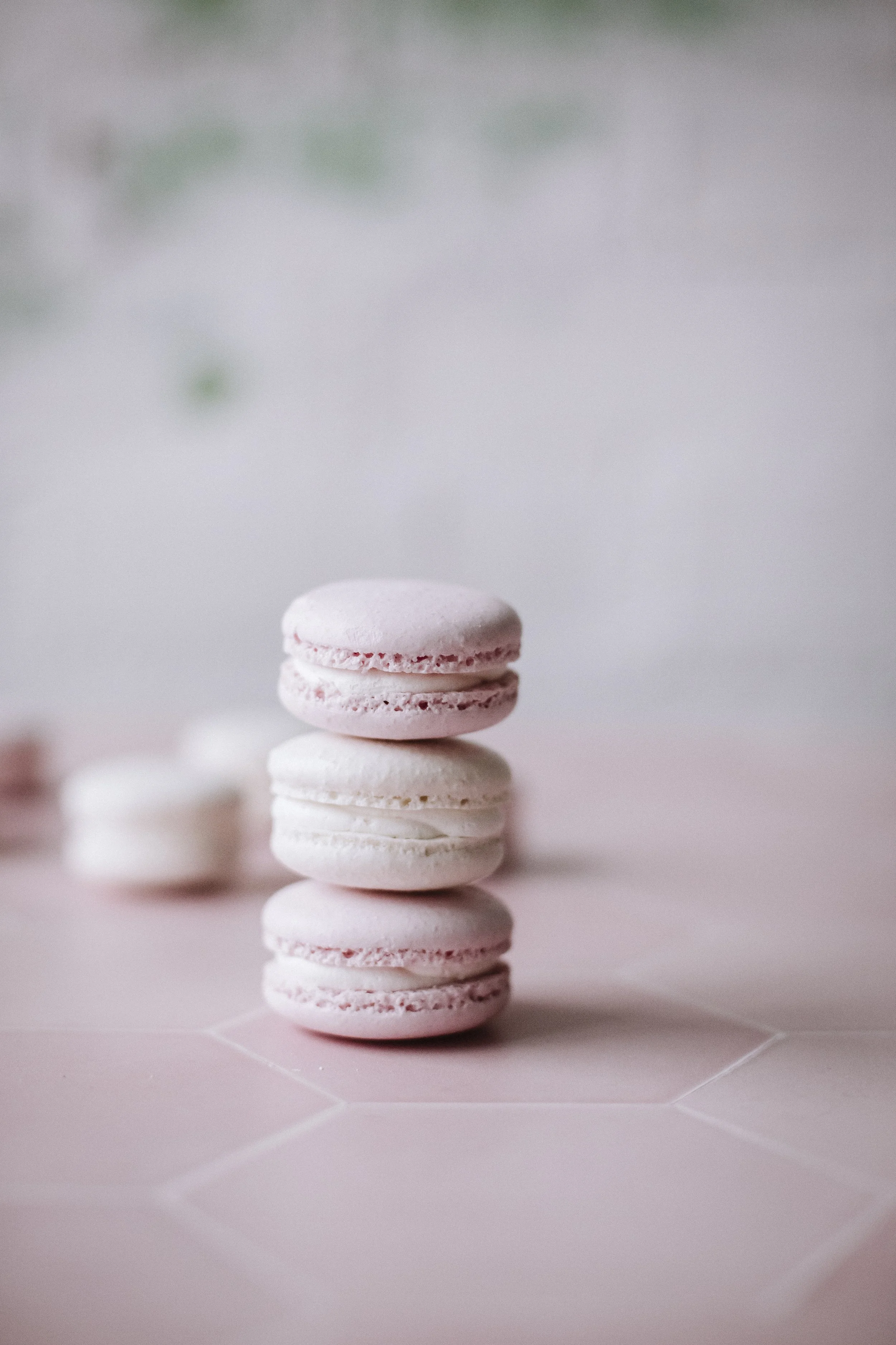 Rivissä neljä vaaleanpunaista ja valkoista makaronia, taustalla hieman muita makaronirenkaita, vaaleanpunaista pintaa.