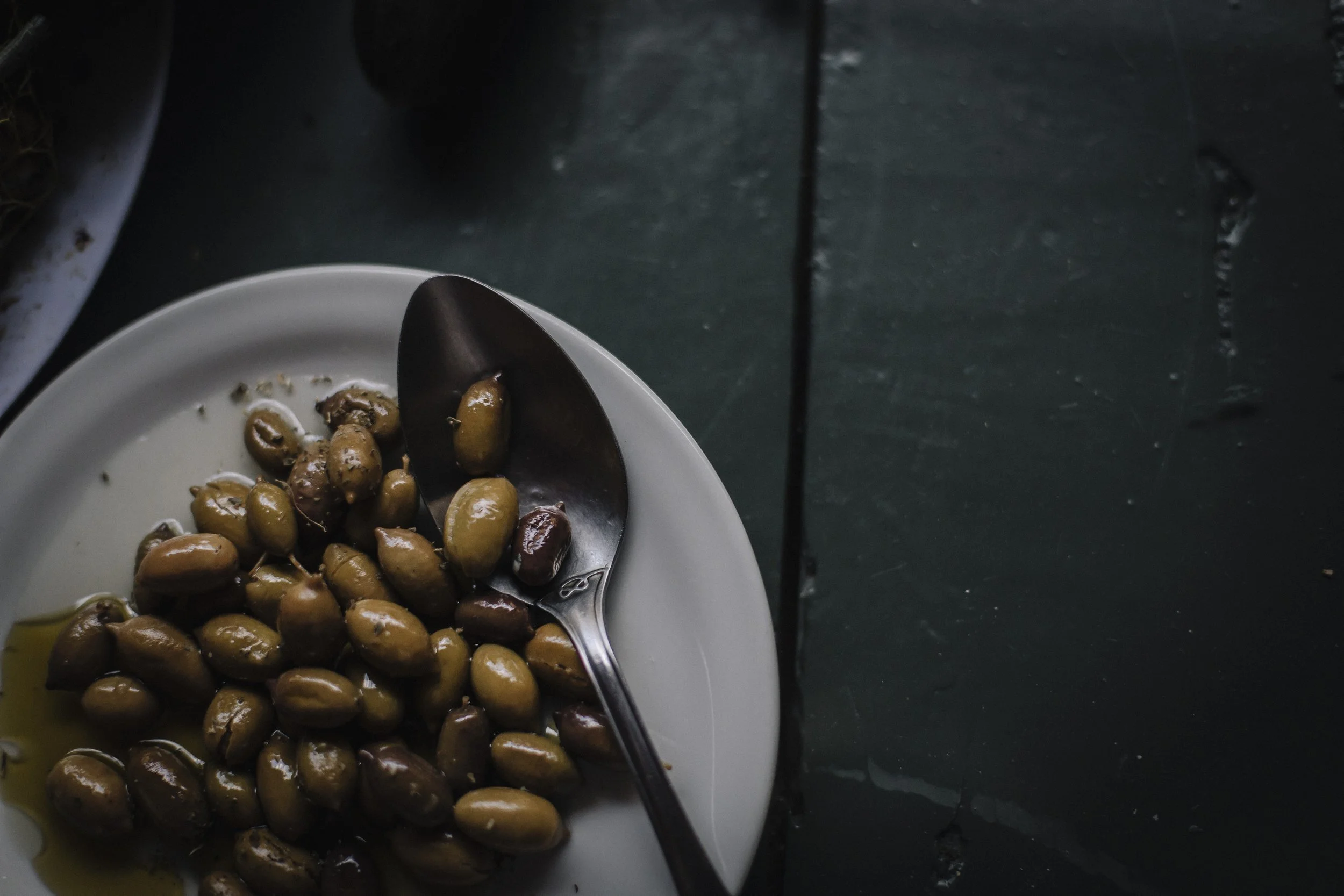 Plate of olives with a spoon on a dark table.