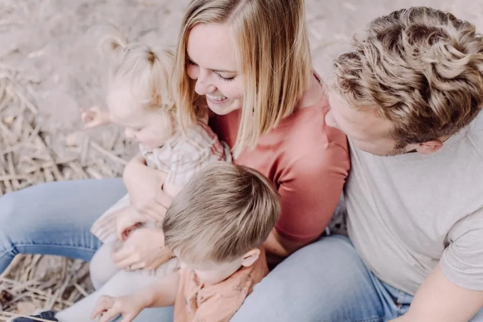 Family of four sitting closely together, smiling and enjoying time outdoors.