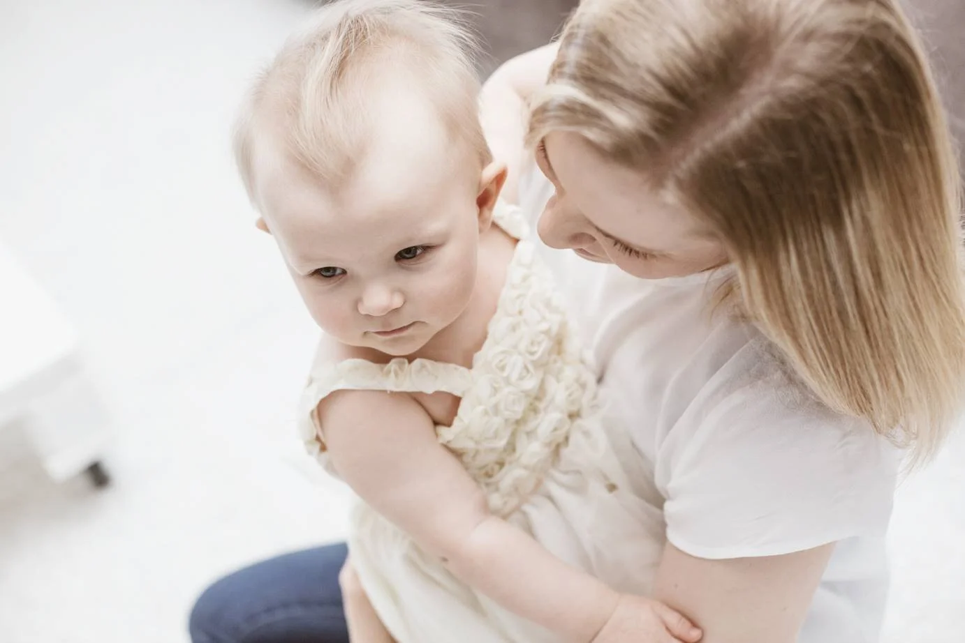 A woman holding a baby, both wearing white clothing, in a tender moment.
