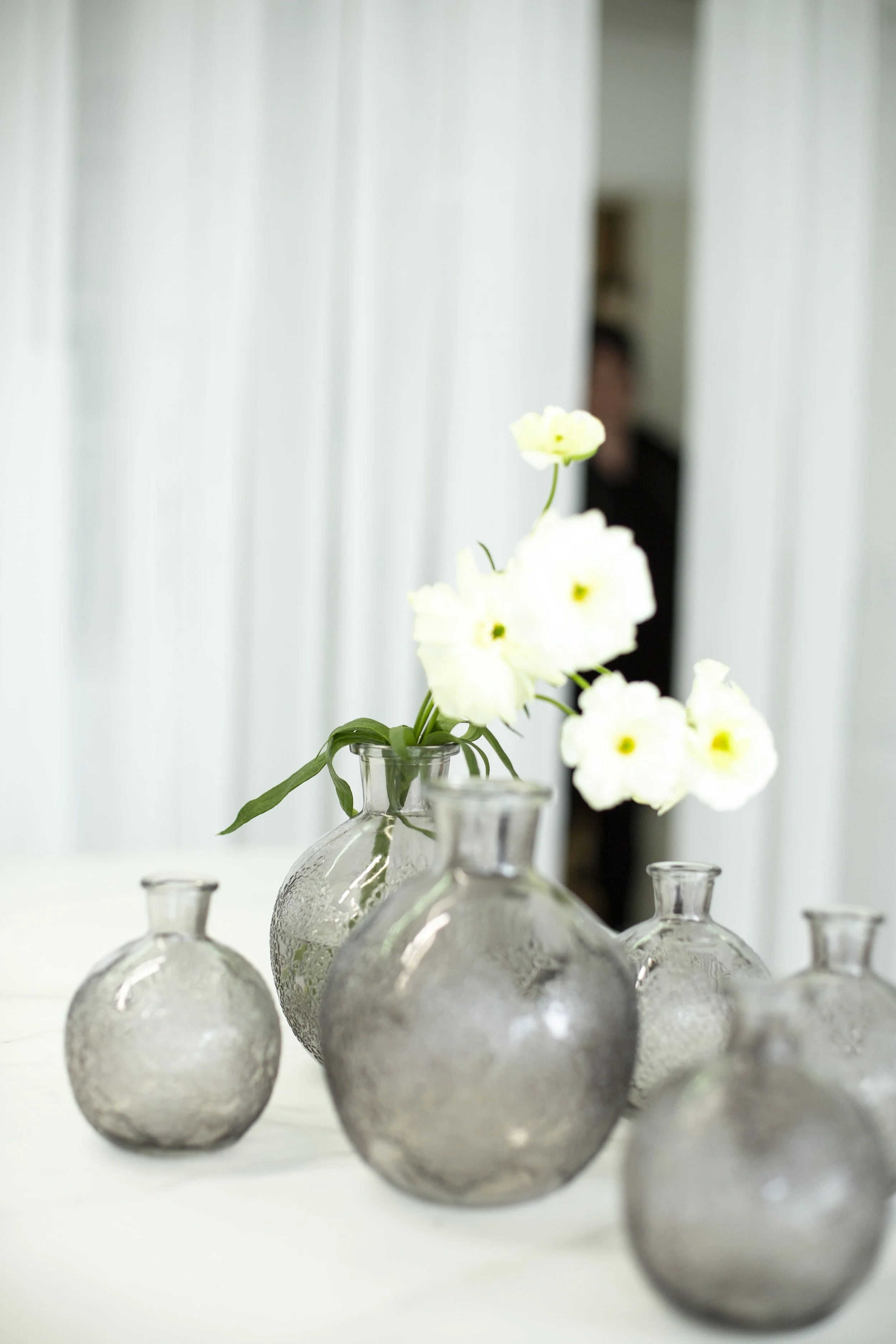 Lasinaluset, joissa on viisi koriste-esinettä, joissa on lasipullot ja valkoisia kukkia.