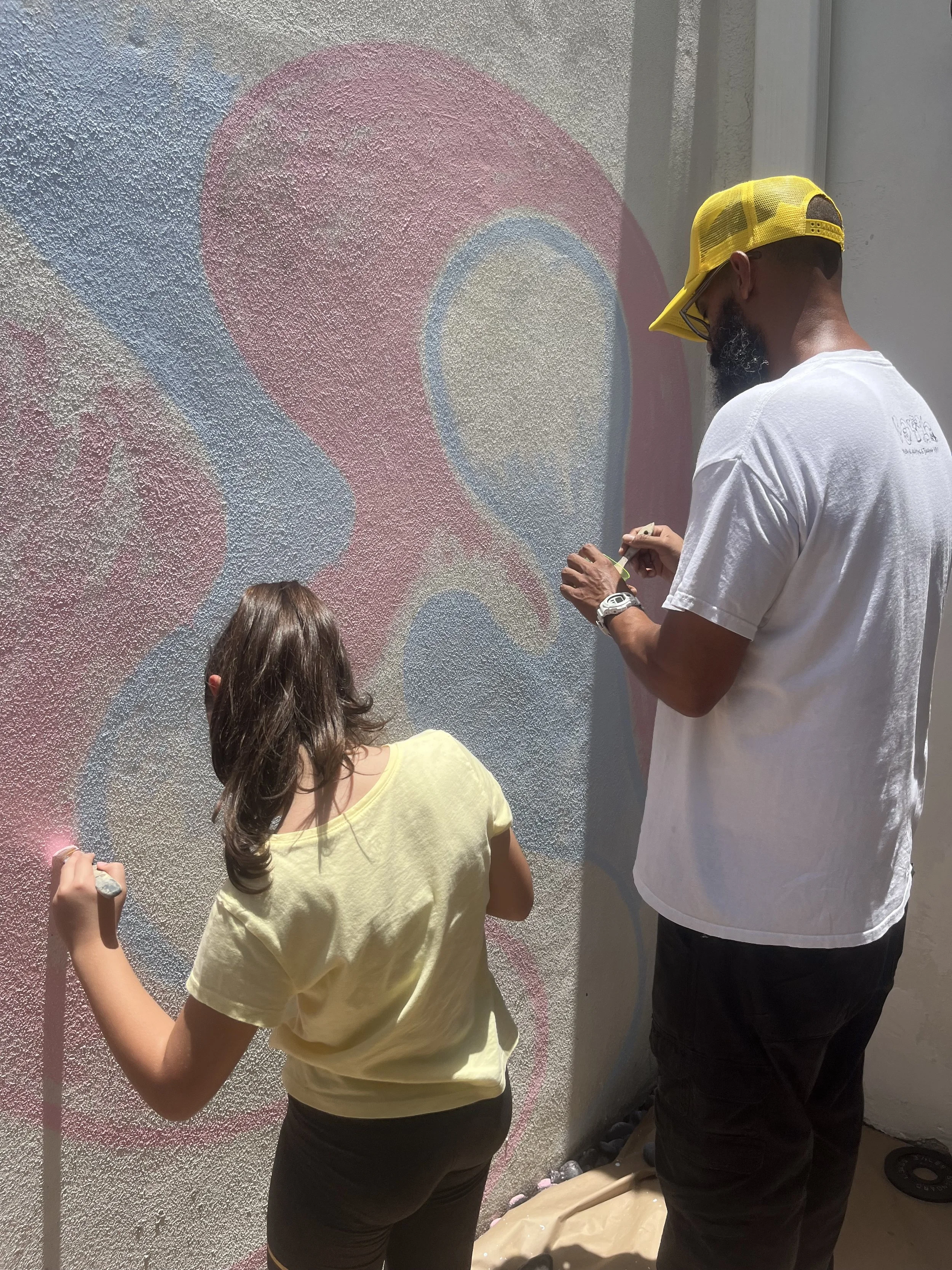 A man and a young girl painting a colorful heart mural on a textured wall. Muse&Flow Miami group custom handmade mural best ideas creative activities corporate team building art workshop Gigi playhouse