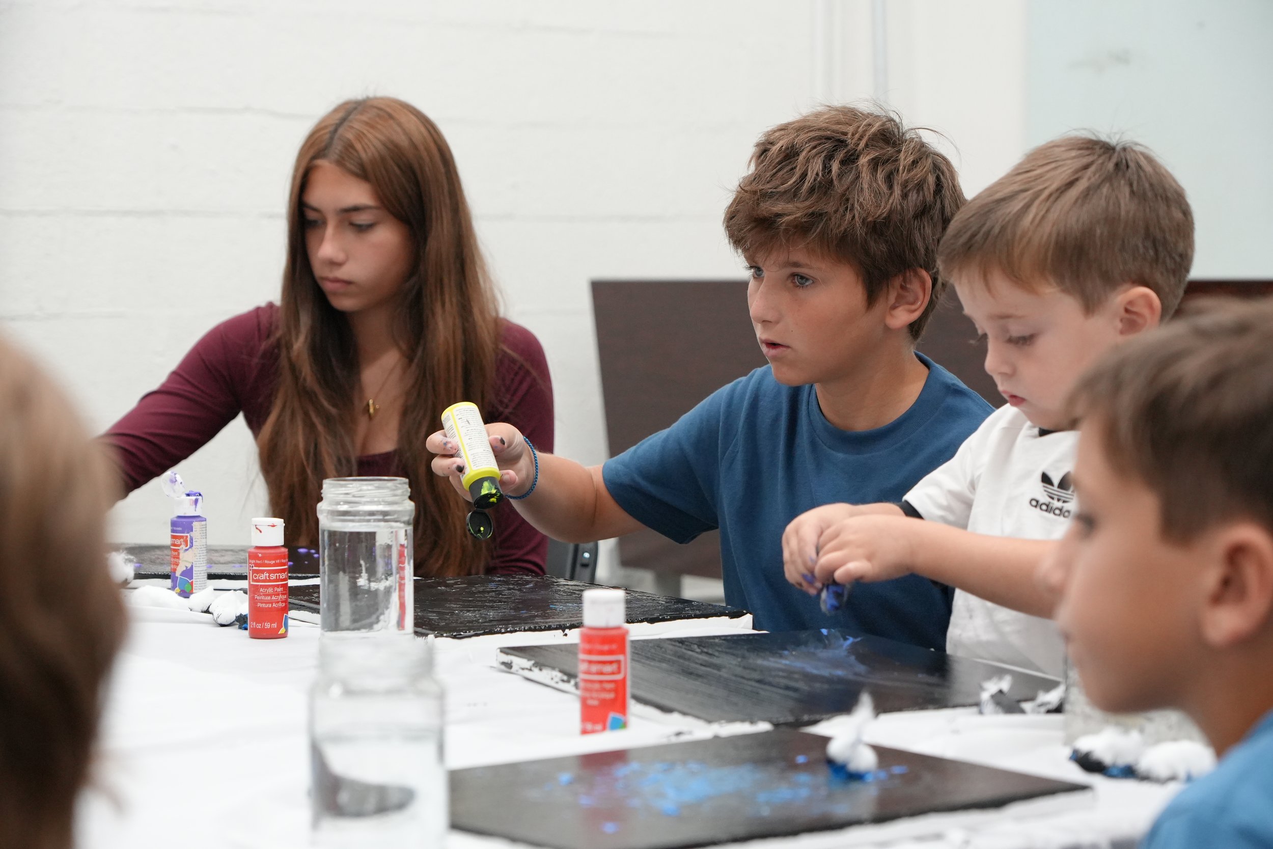 Children participating in an arts and crafts activity at a table, with various craft supplies like glue and paints visible.