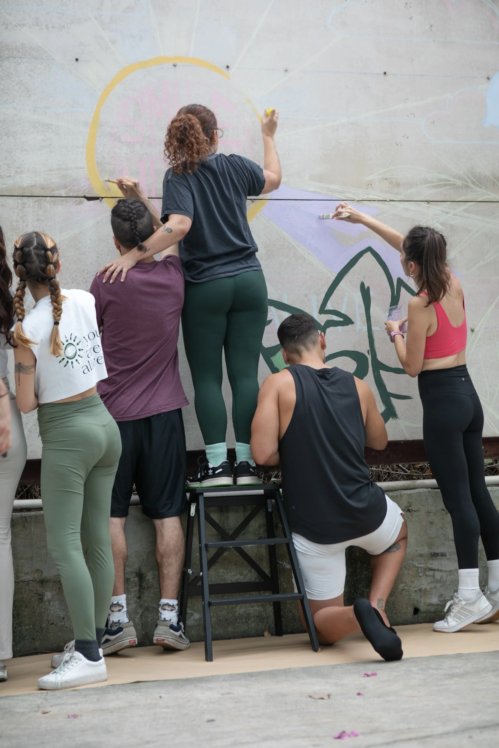 Muse&Flow Miami group custom handmade mural best ideas creative activities corporate team building art workshop Smile Human Ironside A group of people creating a mural on a wall outdoors.