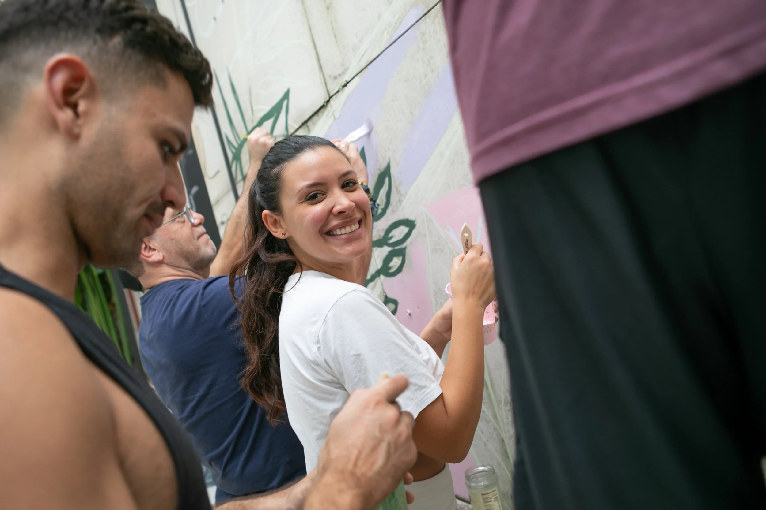 Muse&Flow Miami group custom handmade mural best ideas creative activities corporate team building art workshop Smile Human Ironside  People painting a mural on a wall, with smiles and focused expressions.
