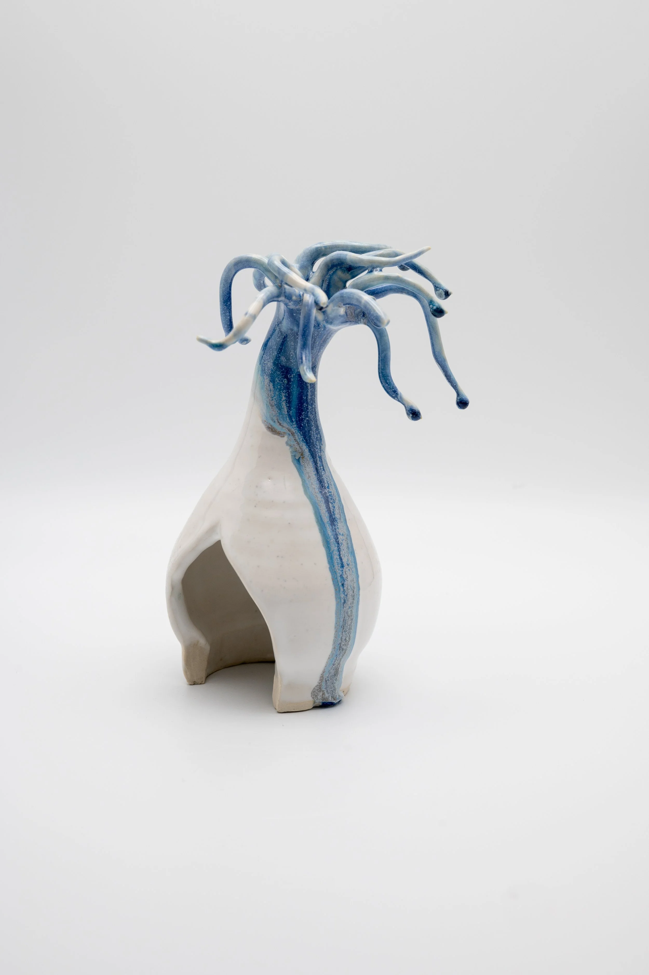 A ceramic vase shaped like an elephant with a hollow opening in its body and a tall, slender neck. A blue and white glazed sculpture with multiple tentacle-like extensions emerges from the top of the elephant's head.