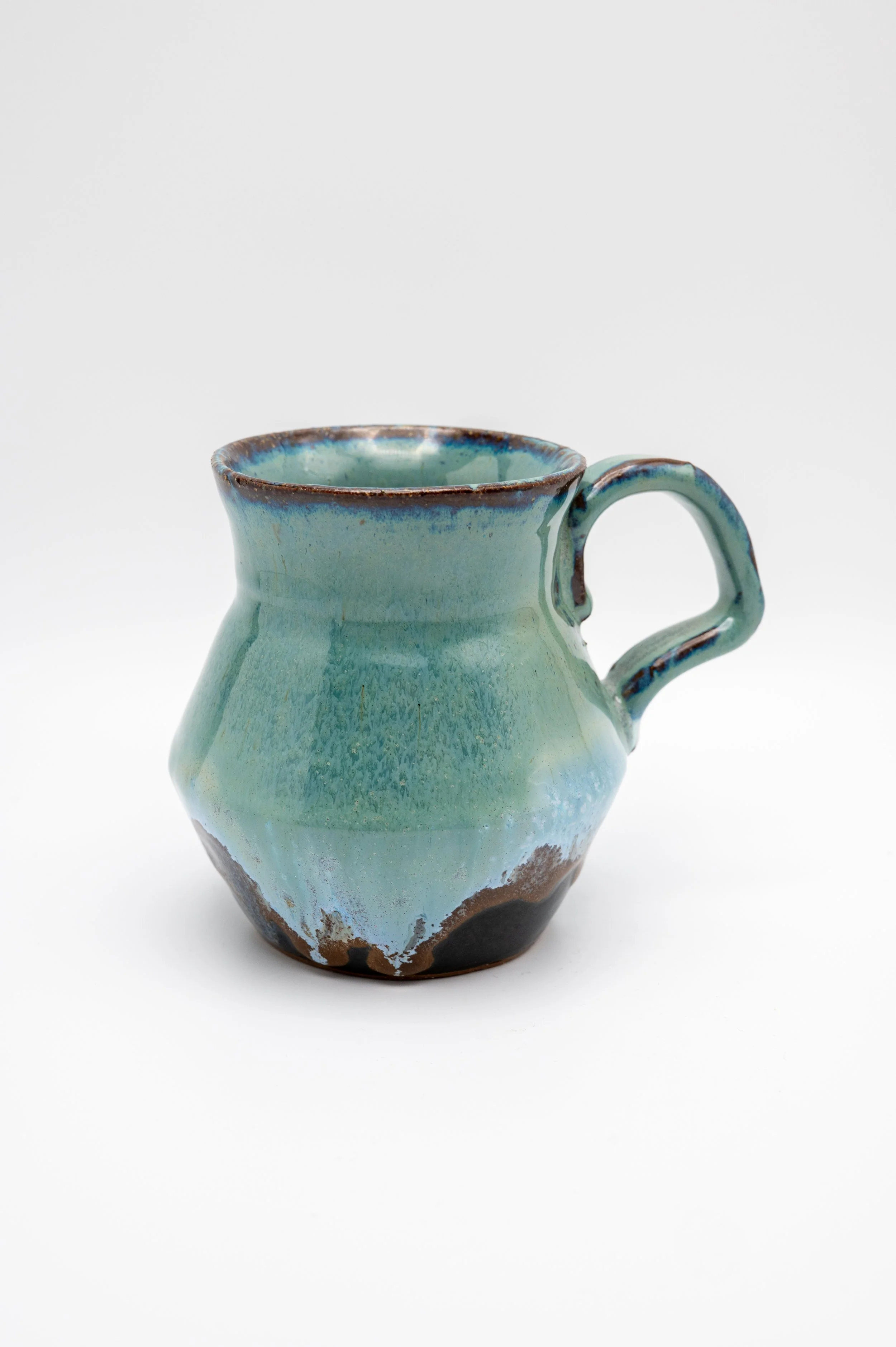 A ceramic pitcher with a rounded body, a narrow opening at the top, and a handle on the side. The pitcher has a glazed finish in shades of blue and green with brown accents near the rim and at the base, and a black area at the bottom.