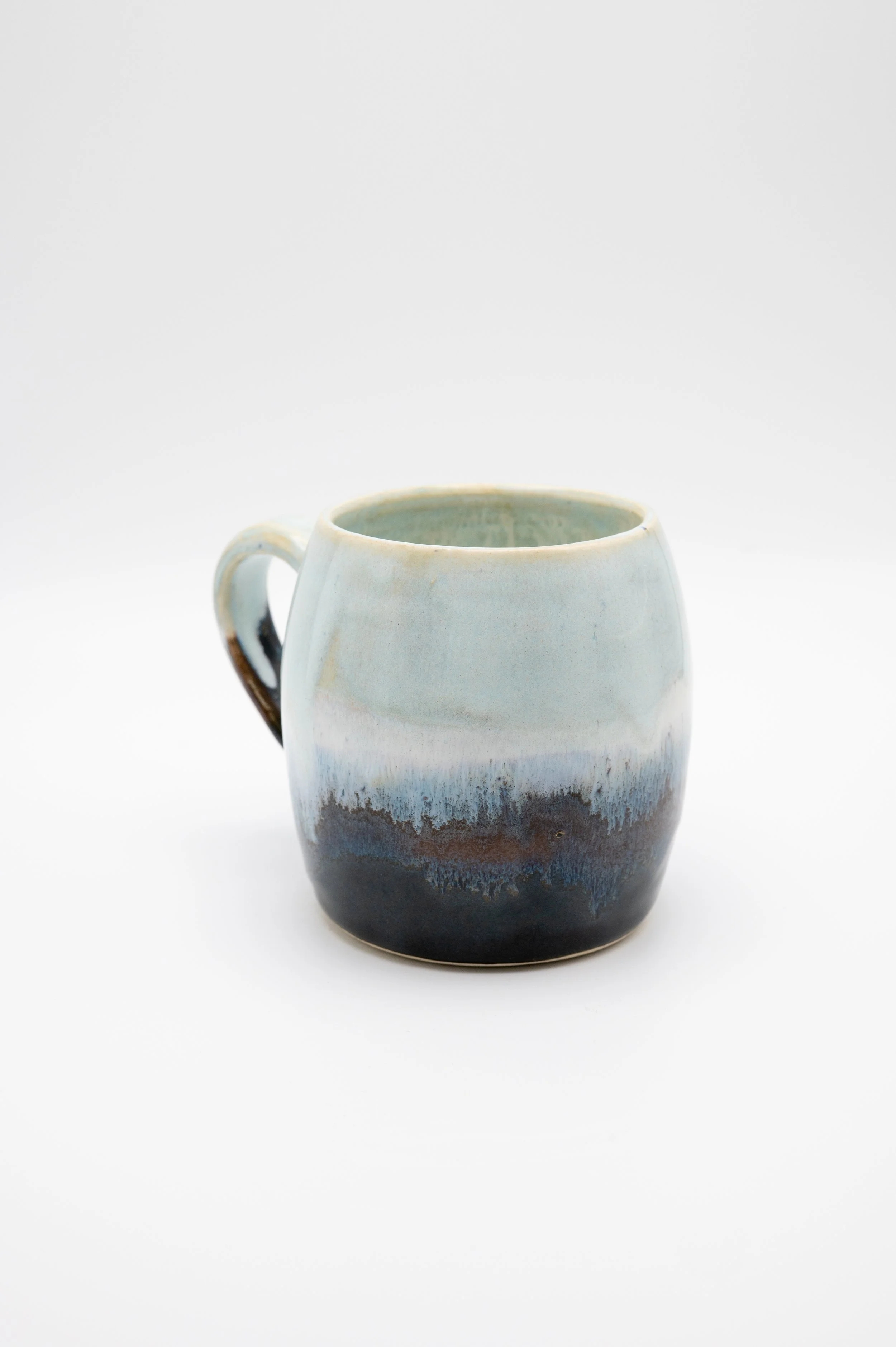 A ceramic mug with a gradient glaze from pale blue at the top to dark blue and brown at the bottom, solo on a white background.