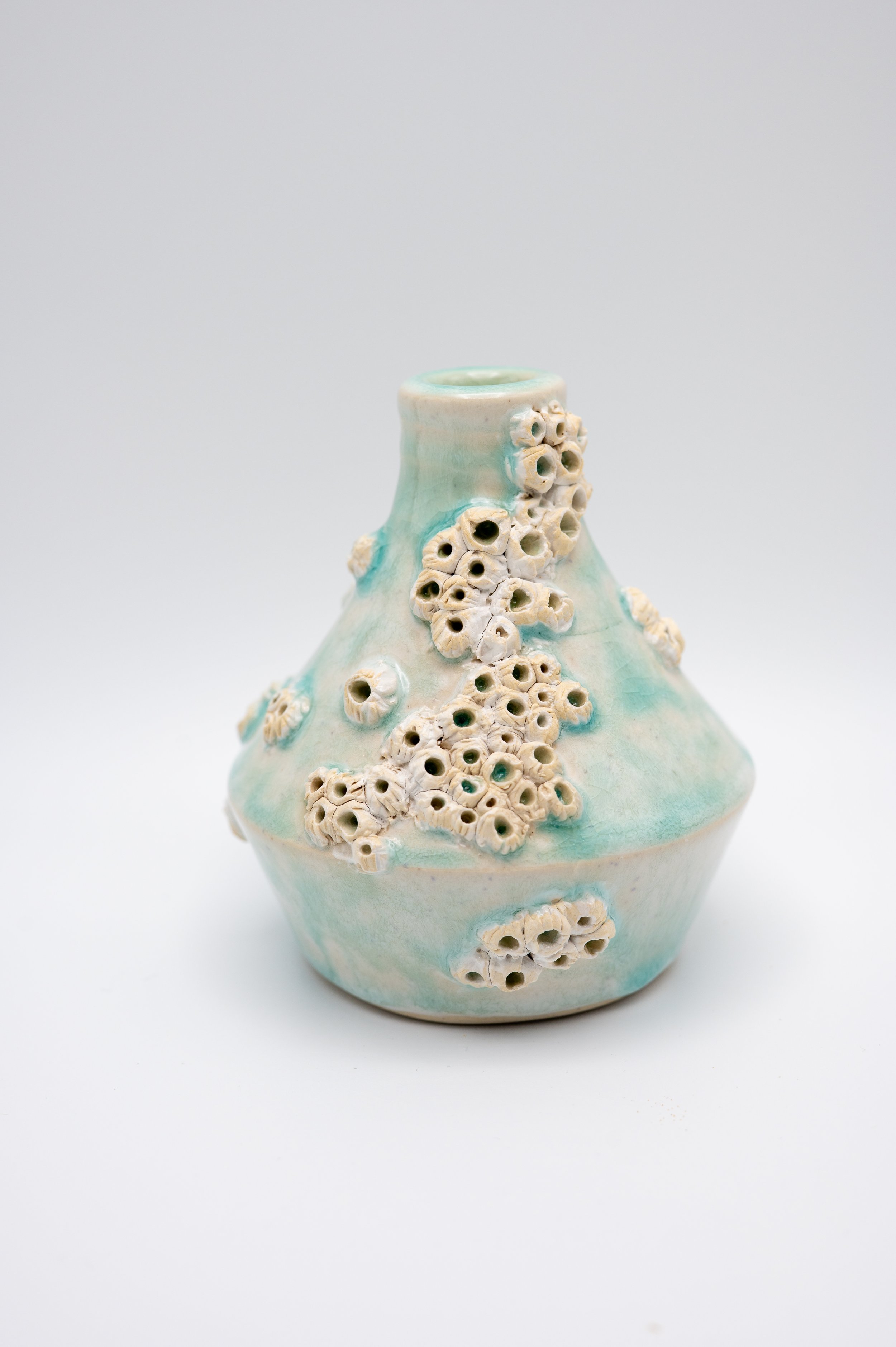 Ceramic vase with a pale turquoise glaze, decorated with clusters of small, white seashell-like protrusions.
