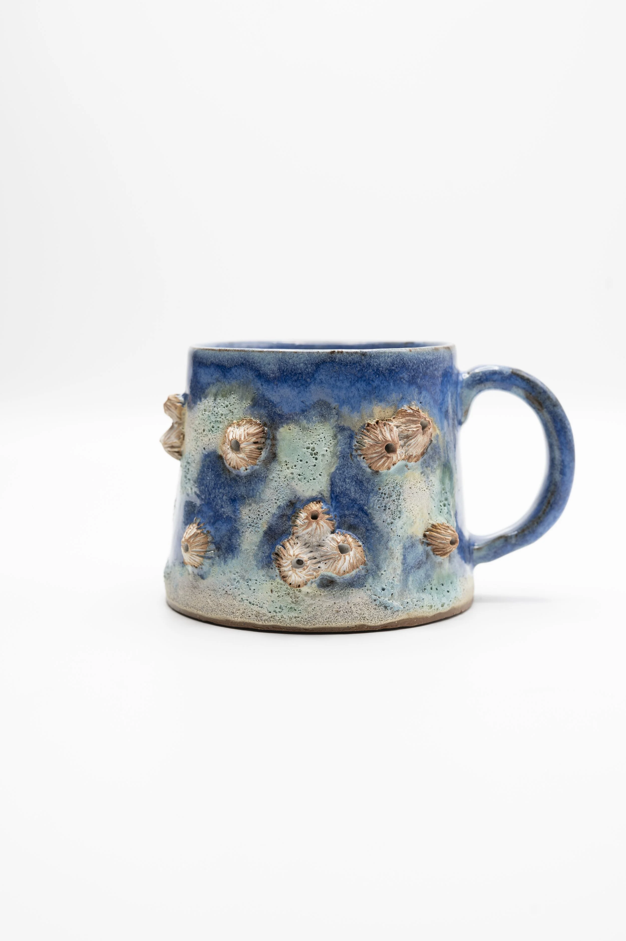 A ceramic mug with a blue glaze and beige textured accents resembling sea creatures, set against a white background.