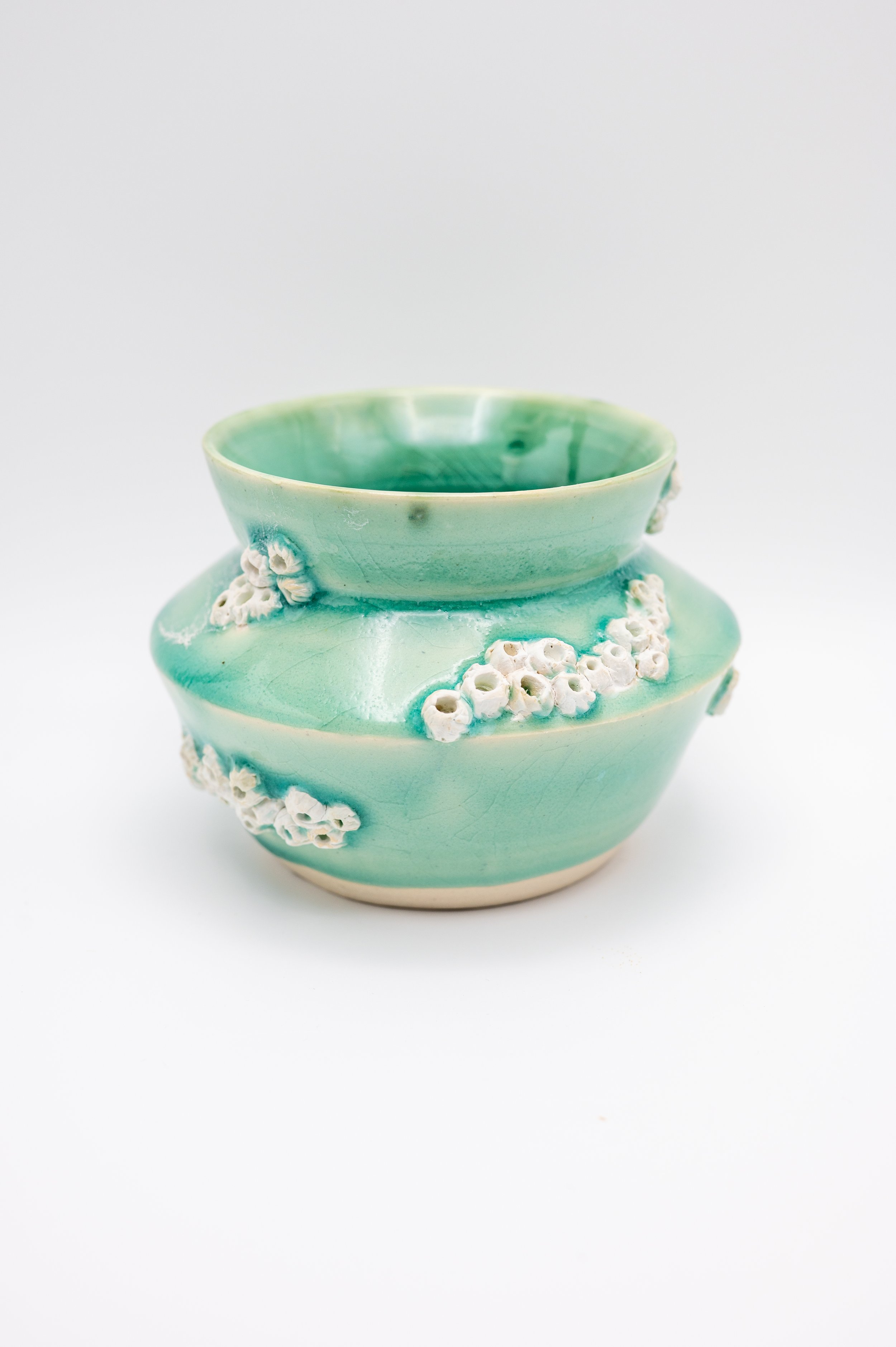 A ceramic vase with a light green glaze, decorated with small white flower-like details around its body, set against a plain white background.