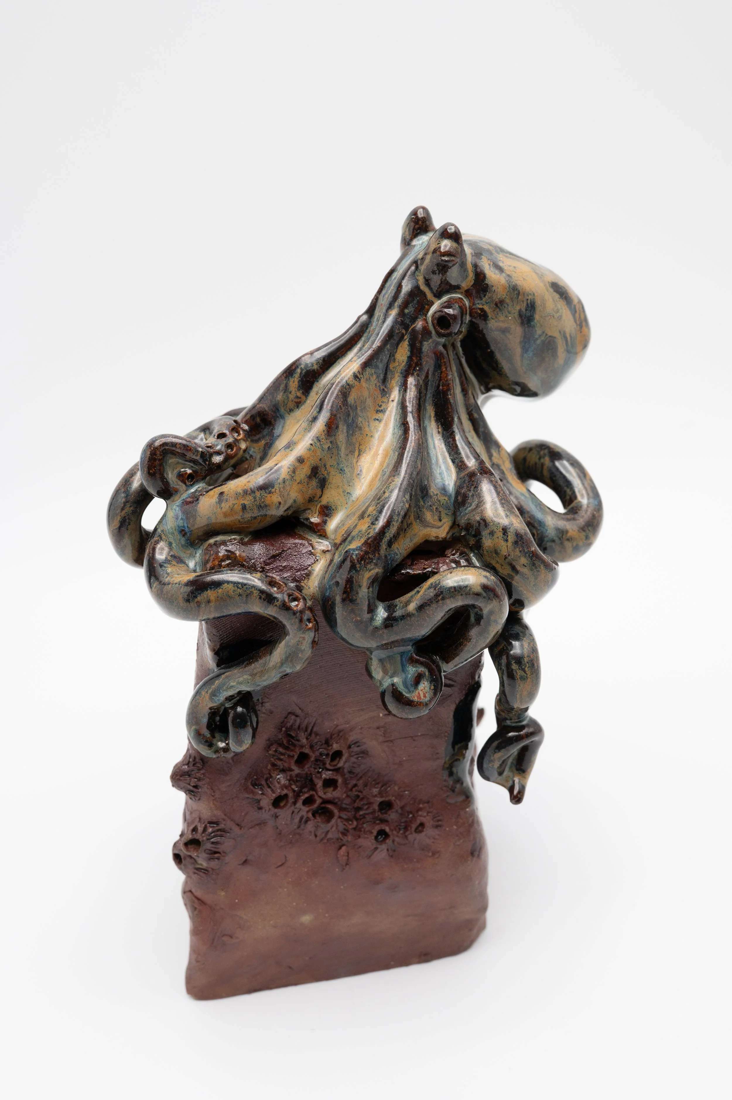 Ceramic sculpture of an octopus with detailed tentacles, mounted on a textured brown base.
