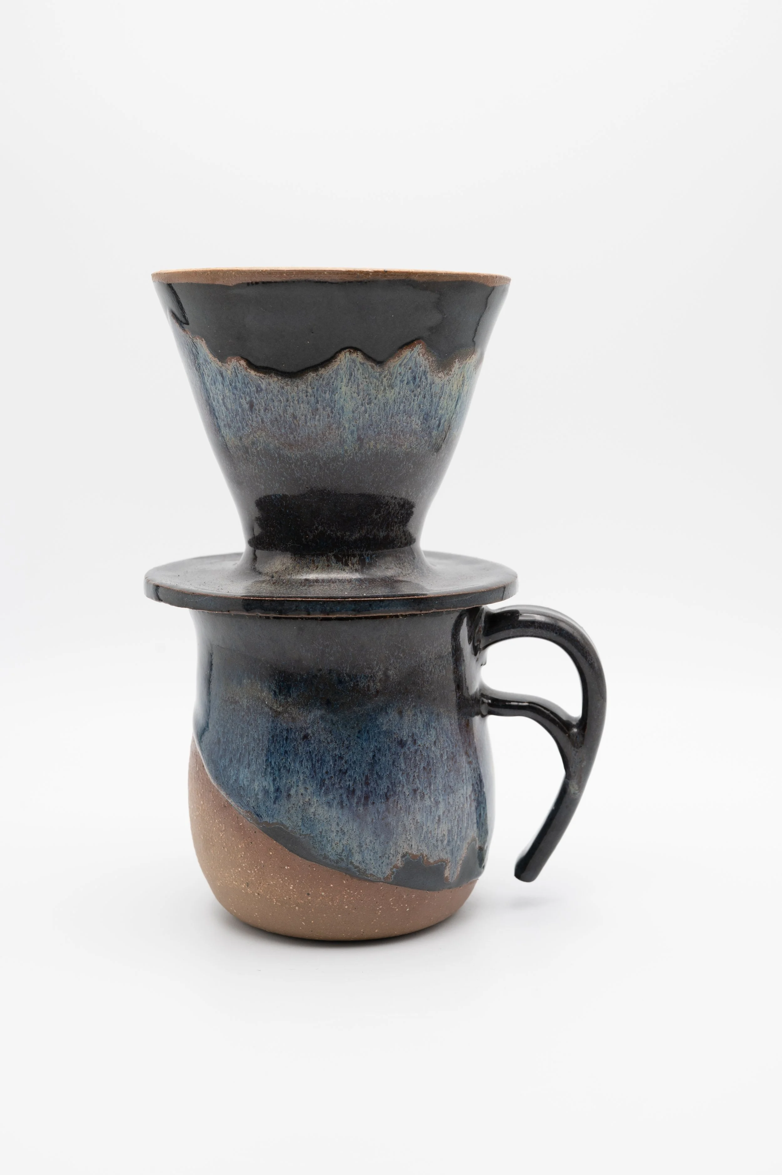 A ceramic coffee cup with a matching lid and a handle, featuring a multicolored, textured glaze with earthy tones and a matte finish, set against a plain white background.