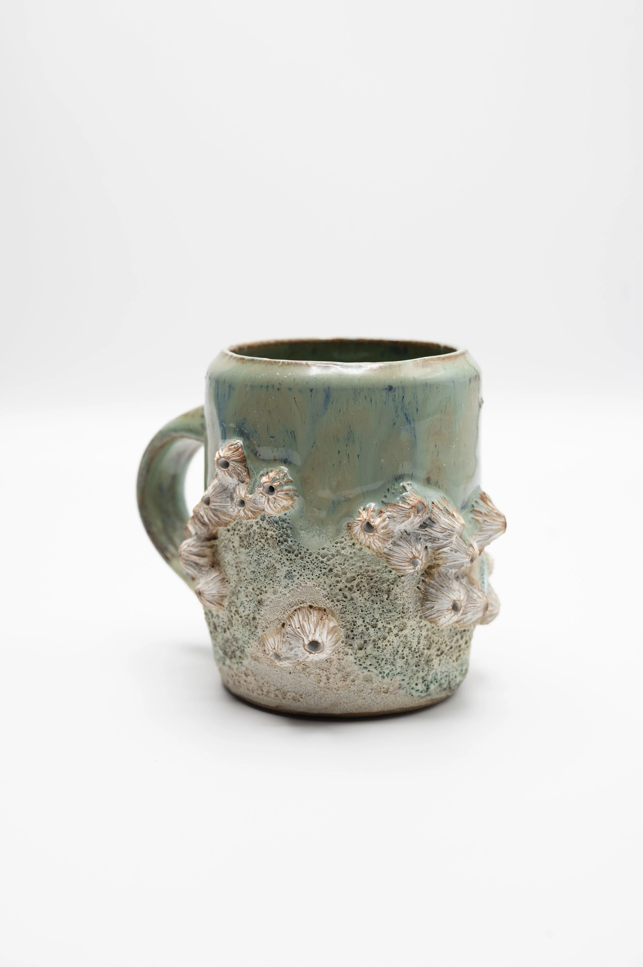 A ceramic mug with a textured base and a smooth, glazed upper portion, decorated with small, detailed flower-like forms around the lower part, set against a plain white background.