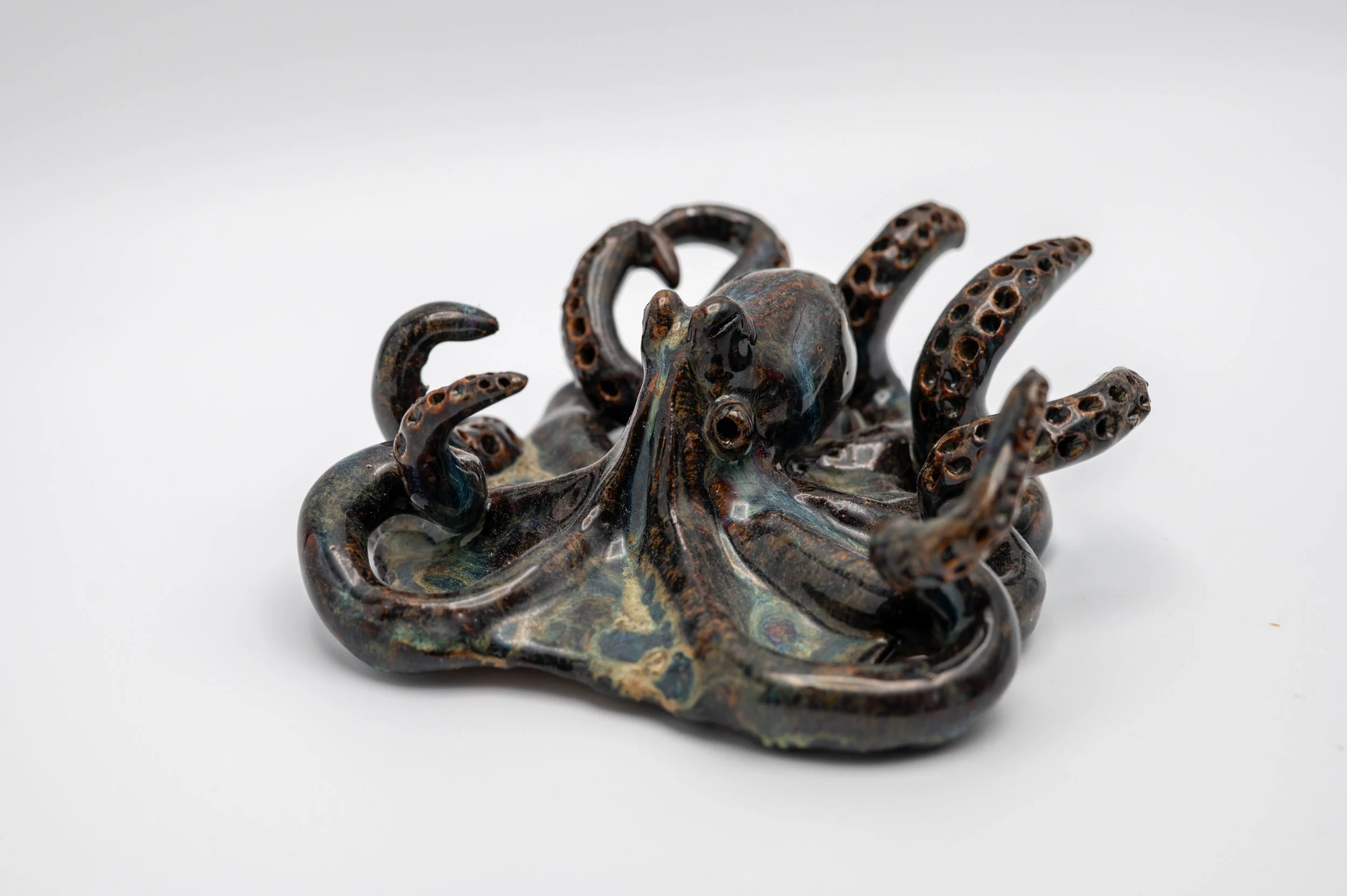 A ceramic sculpture of a swirling octopus with detailed tentacles on a plain white background.