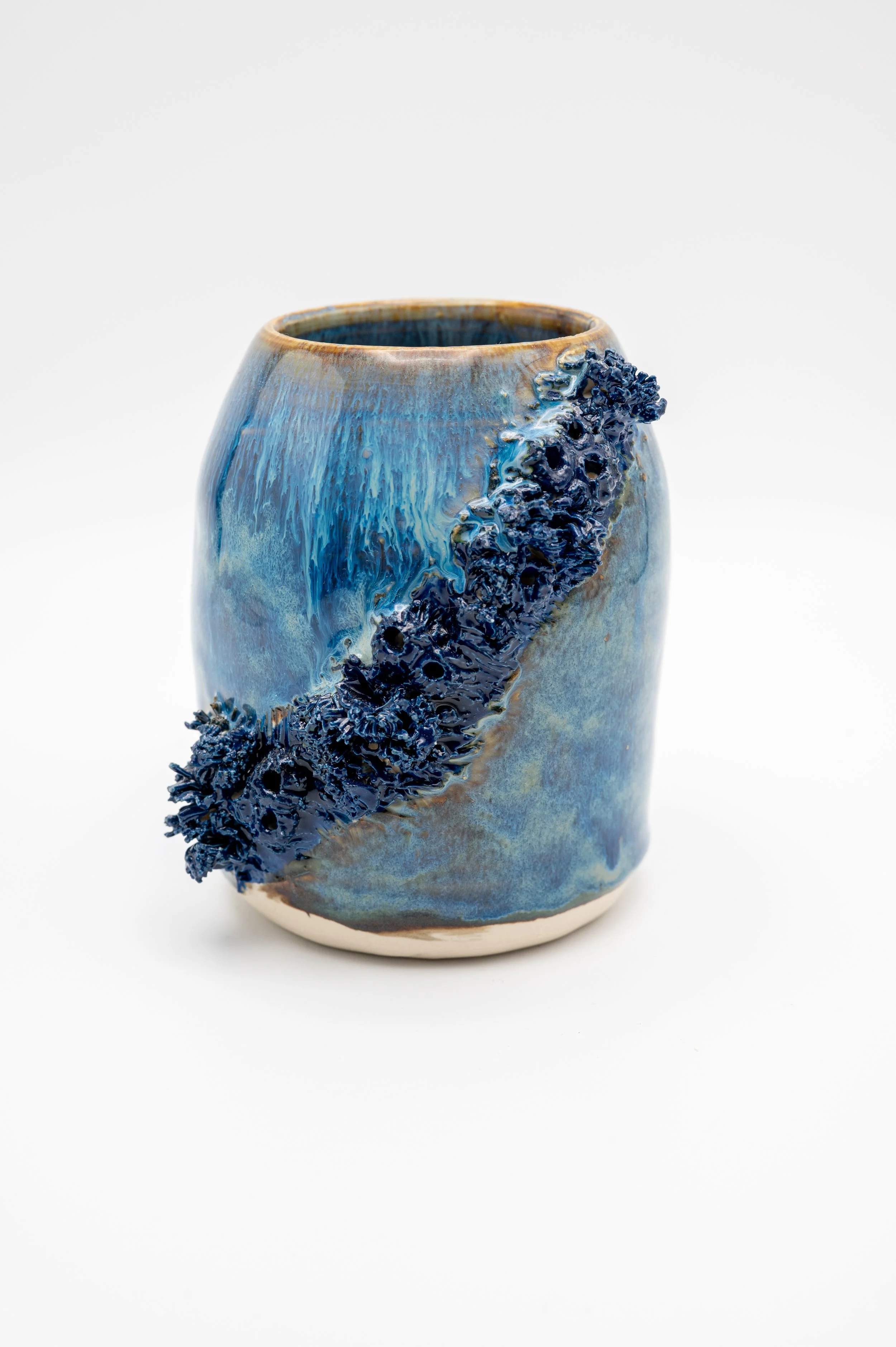 A ceramic vase with a textured, dark blue pattern on its side, featuring a glaze in shades of blue and brown, against a plain white background.