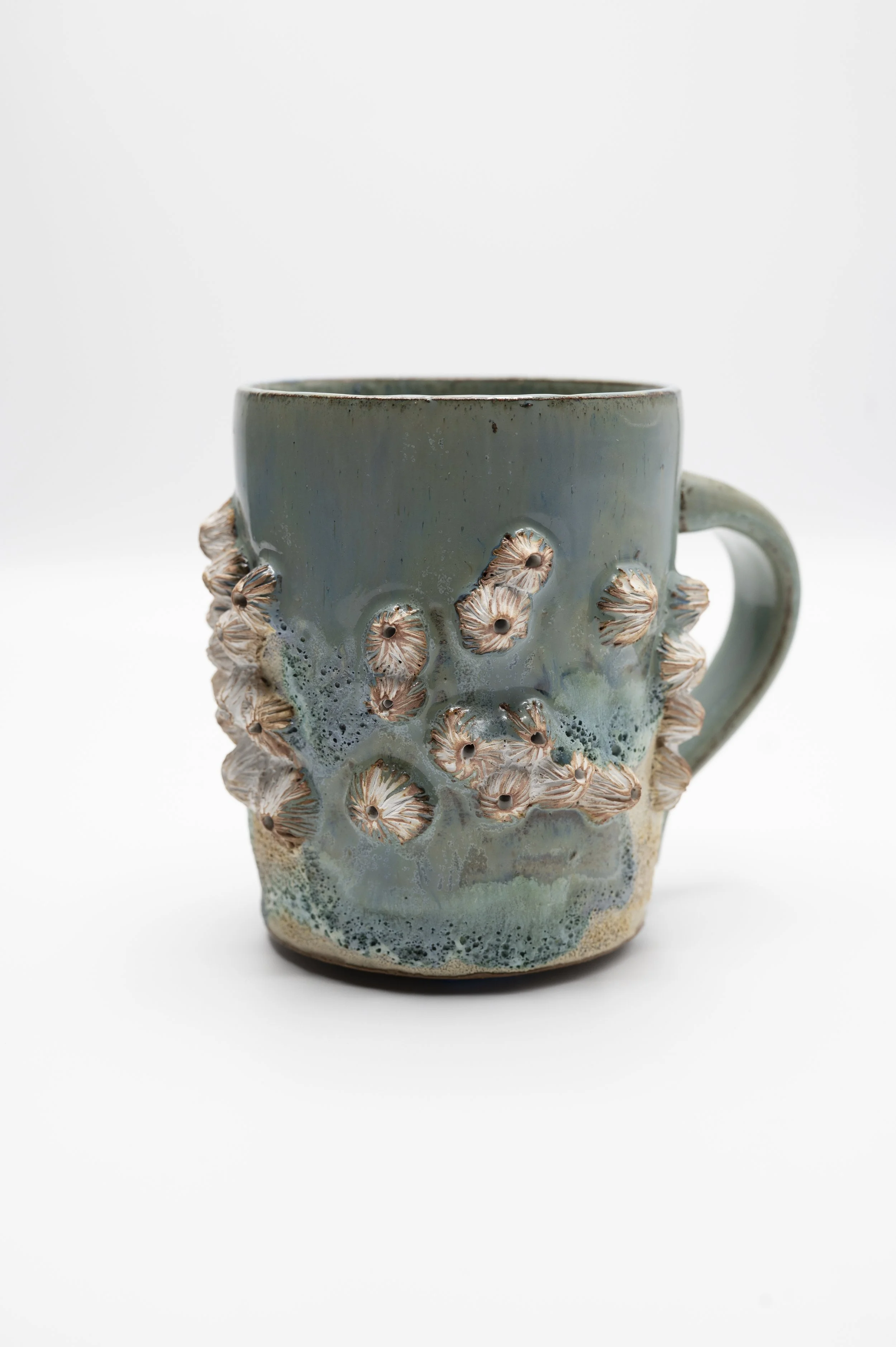 A ceramic mug with a textured exterior featuring small coral-like designs, glazed in shades of blue and beige, set against a plain white background.