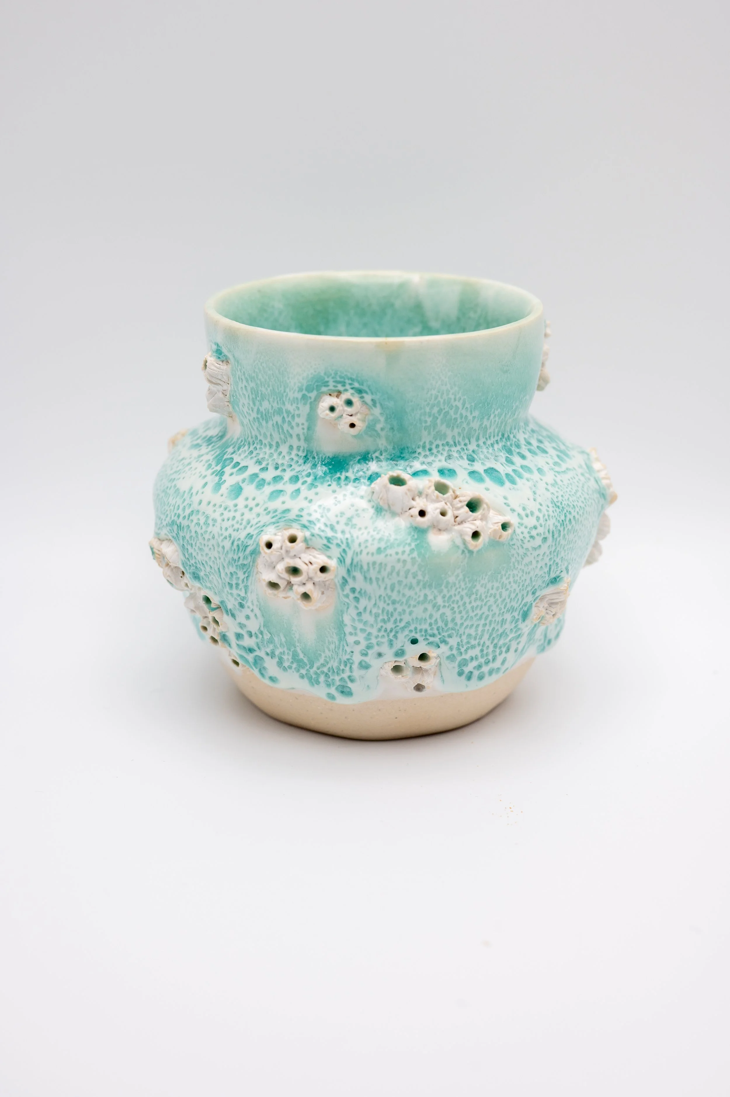 Ceramic vase with a textured turquoise glaze and white accents, featuring small holes and protrusions, on a white background.