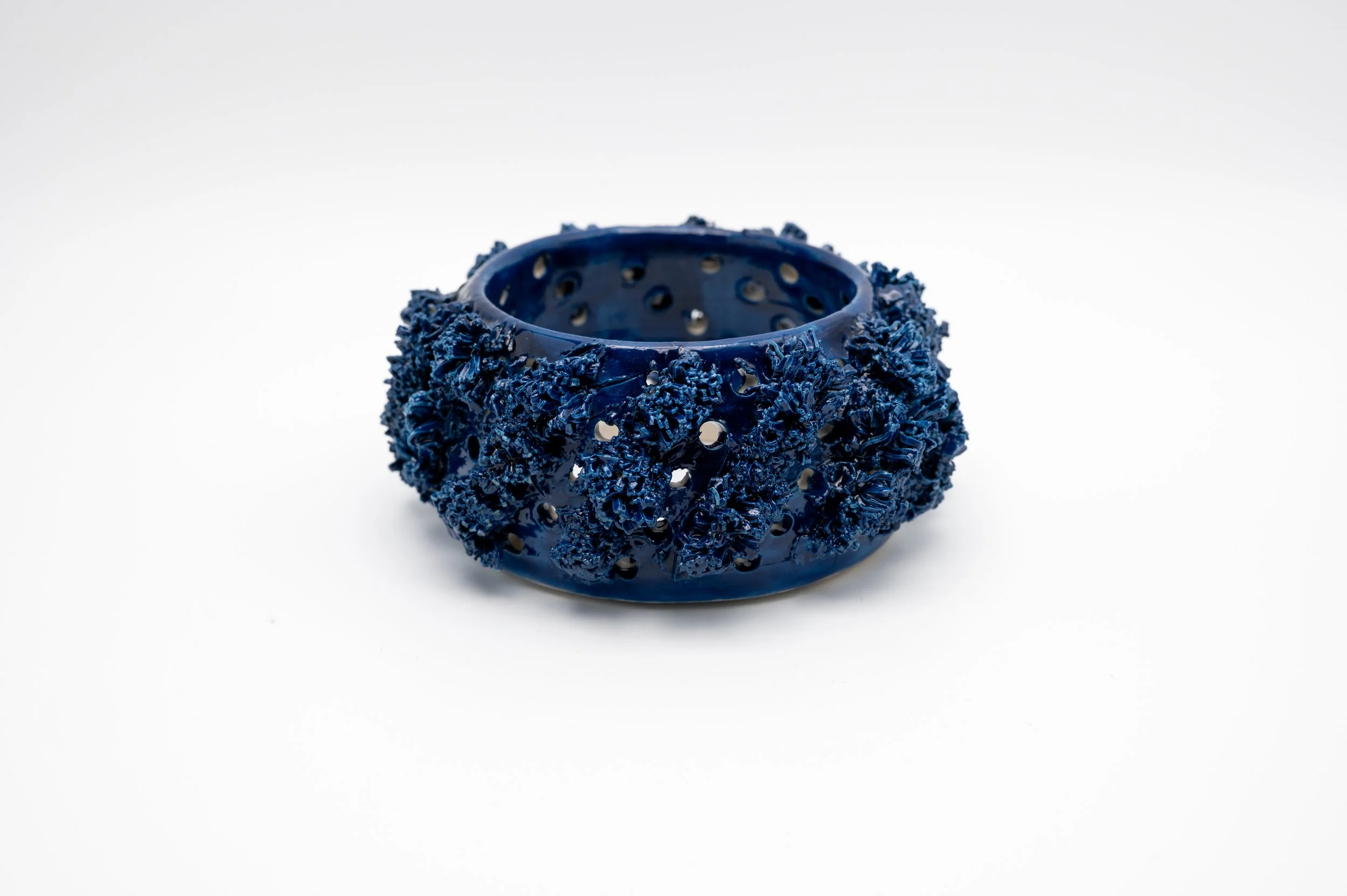 A dark blue, textured, open-ring sculpture with an intricate, ruffled surface, placed on a white background.
